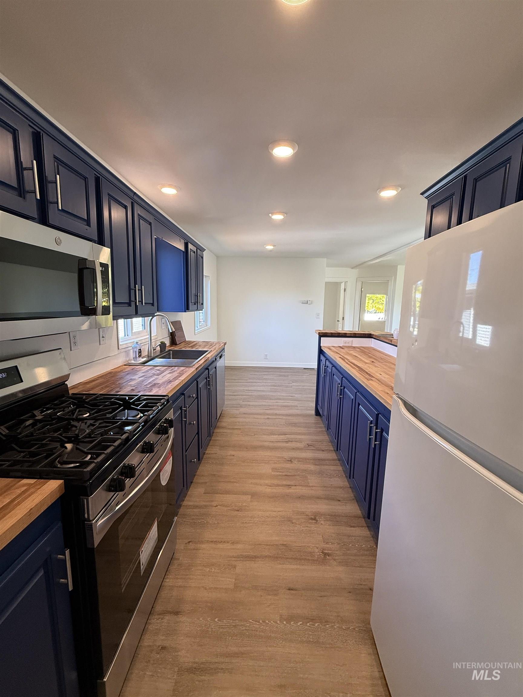Kitchen featuring stainless steel appliances, butcher block countertops, light wood finished floors, blue cabinets, and recessed lighting