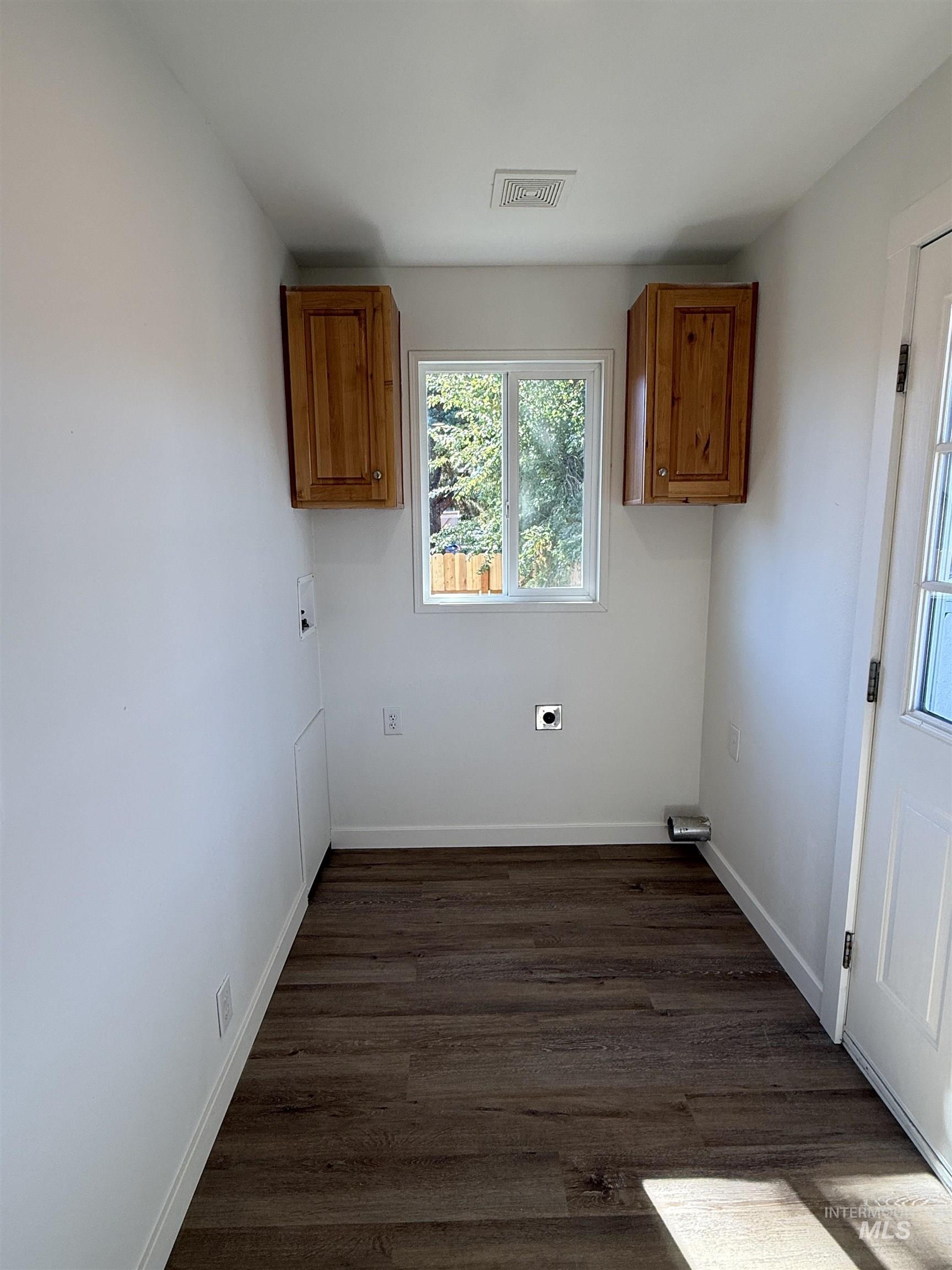 Laundry room with electric dryer hookup, dark wood finished floors, and cabinet space