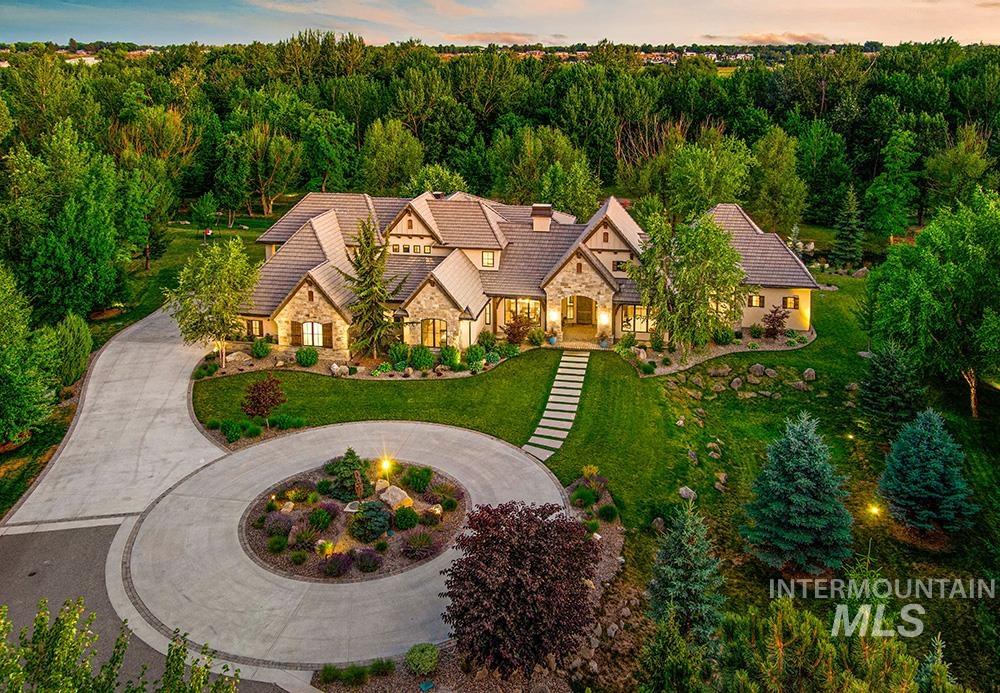 View of front of house featuring stone siding, curved driveway, a chimney, a lawn, and a view of trees