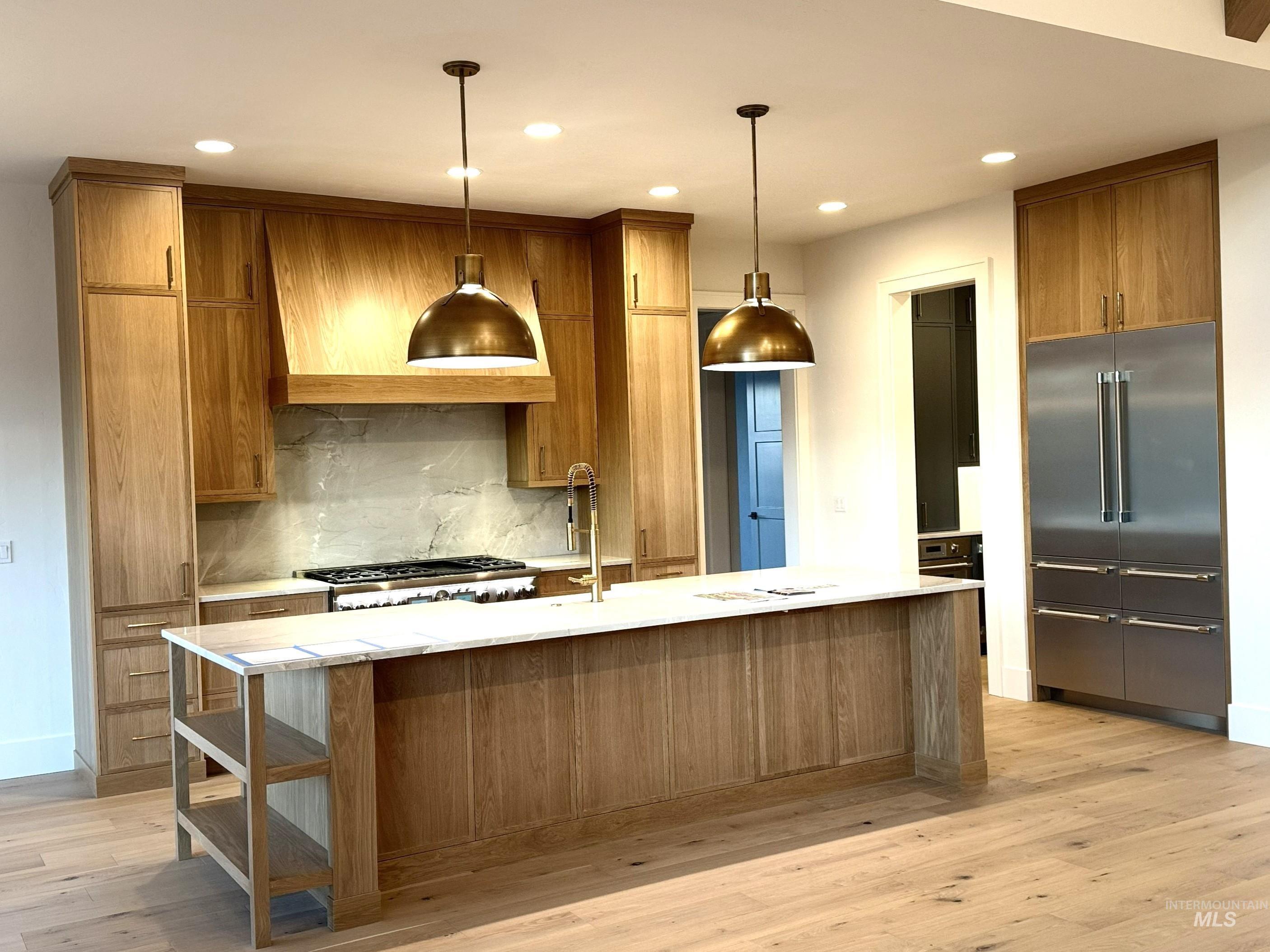 Kitchen featuring brown cabinetry, tasteful backsplash, appliances with stainless steel finishes, light stone counters, and light wood-style floors