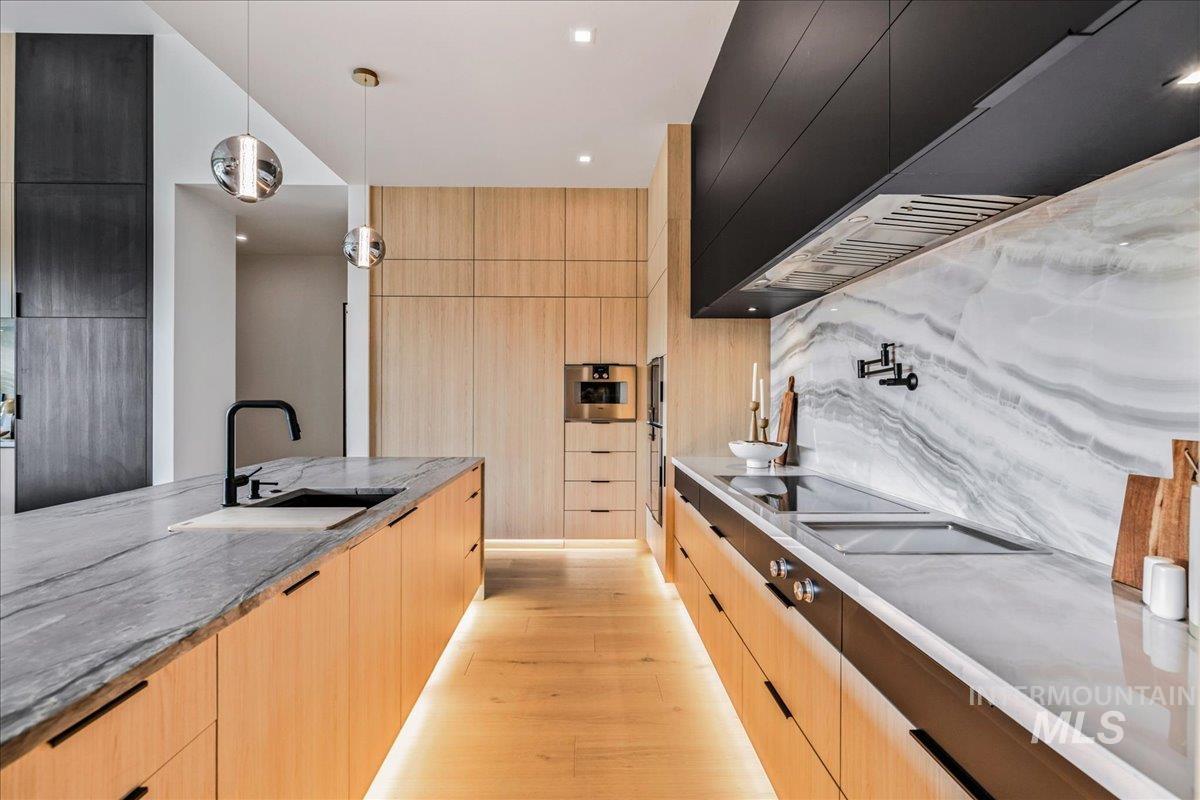 Kitchen with premium range hood, pendant lighting, light stone counters, modern cabinets, and light brown cabinetry