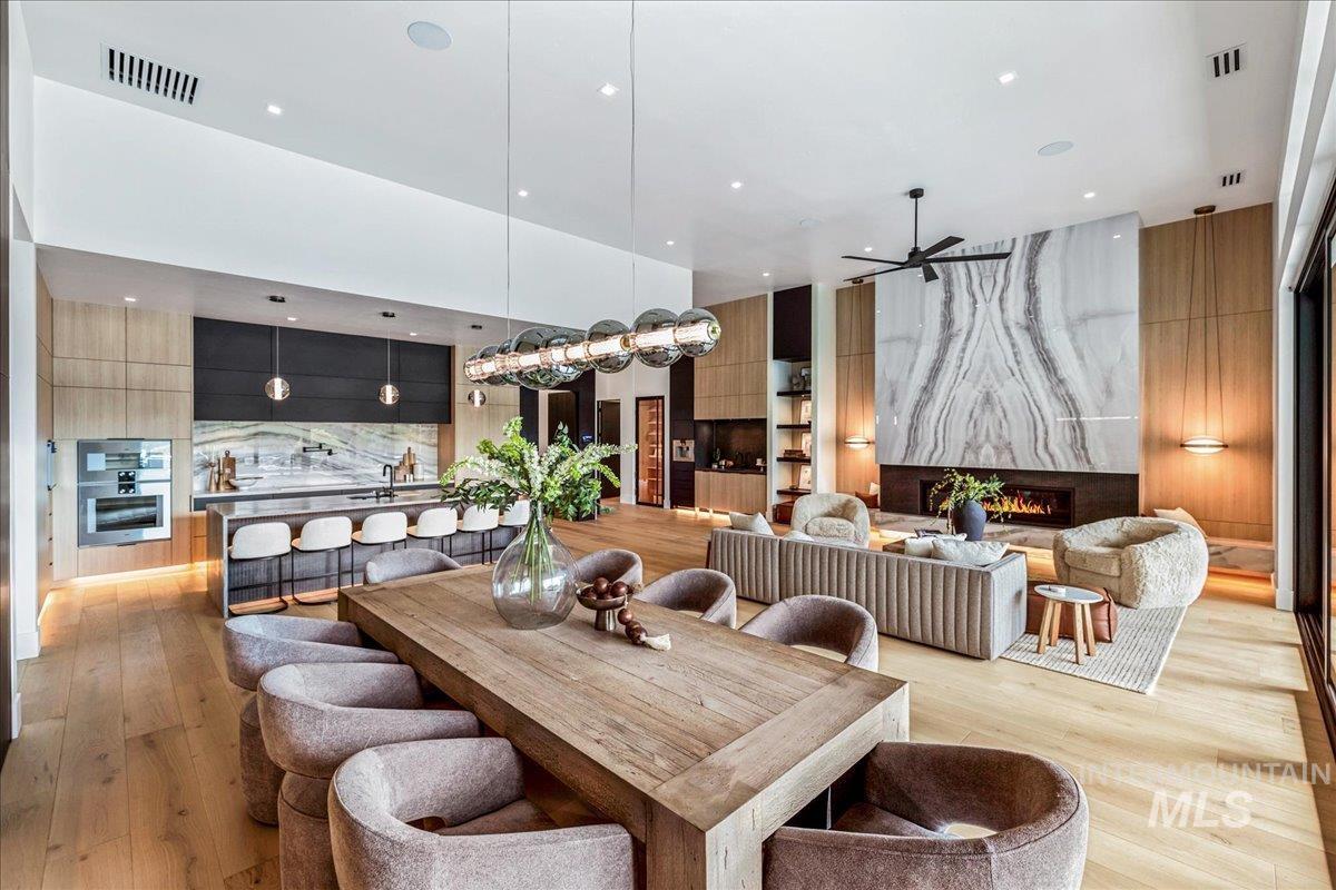 Dining room with a fireplace, light wood finished floors, recessed lighting, ceiling fan, and a towering ceiling