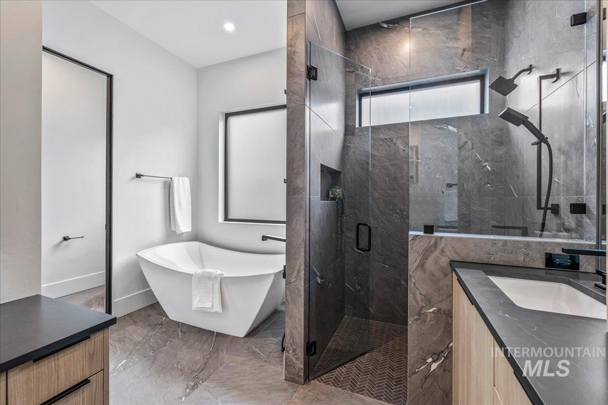 Bathroom with vanity, a freestanding bath, a marble finish shower, and light marble finish floors