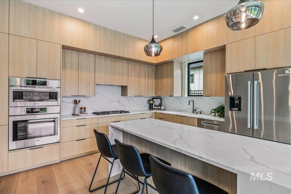 Kitchen with modern cabinets, light stone counters, pendant lighting, and stainless steel appliances