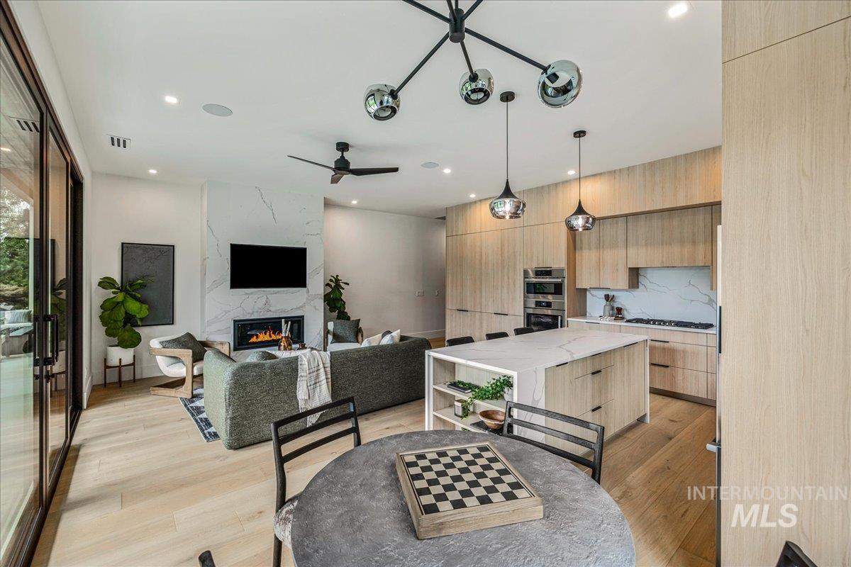 Dining room with light wood-style flooring, a ceiling fan, a premium fireplace, and recessed lighting