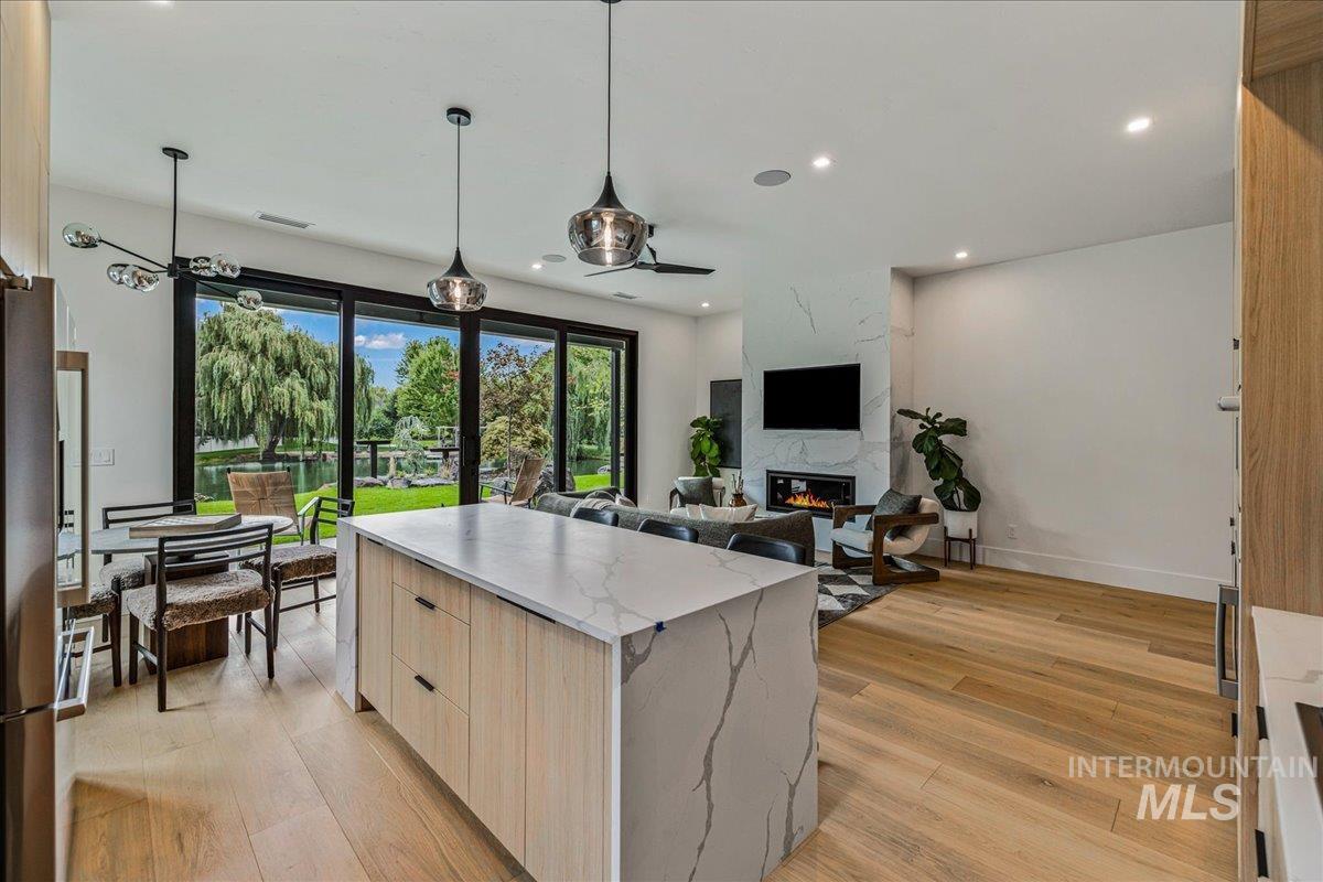 Kitchen featuring light wood-type flooring, pendant lighting, light brown cabinetry, a premium fireplace, and freestanding refrigerator