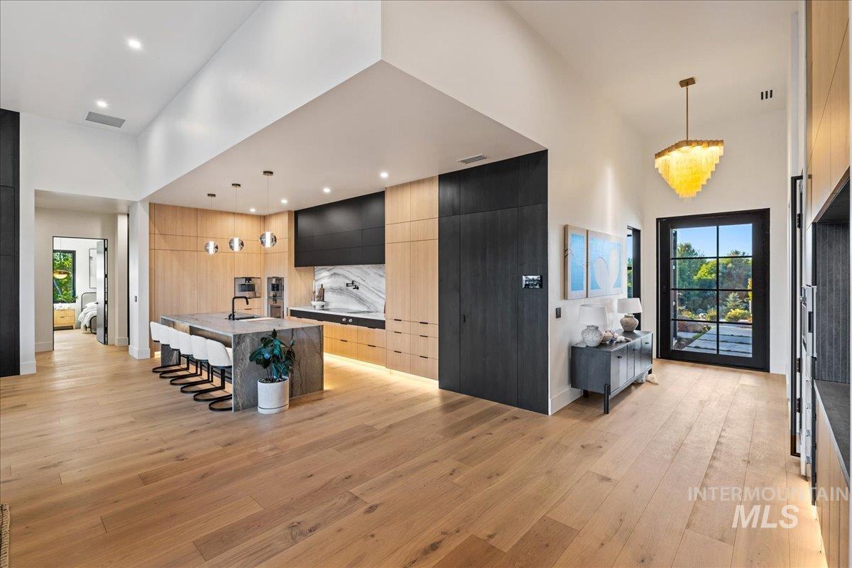 Kitchen with a kitchen breakfast bar, decorative light fixtures, a kitchen island with sink, modern cabinets, and a towering ceiling