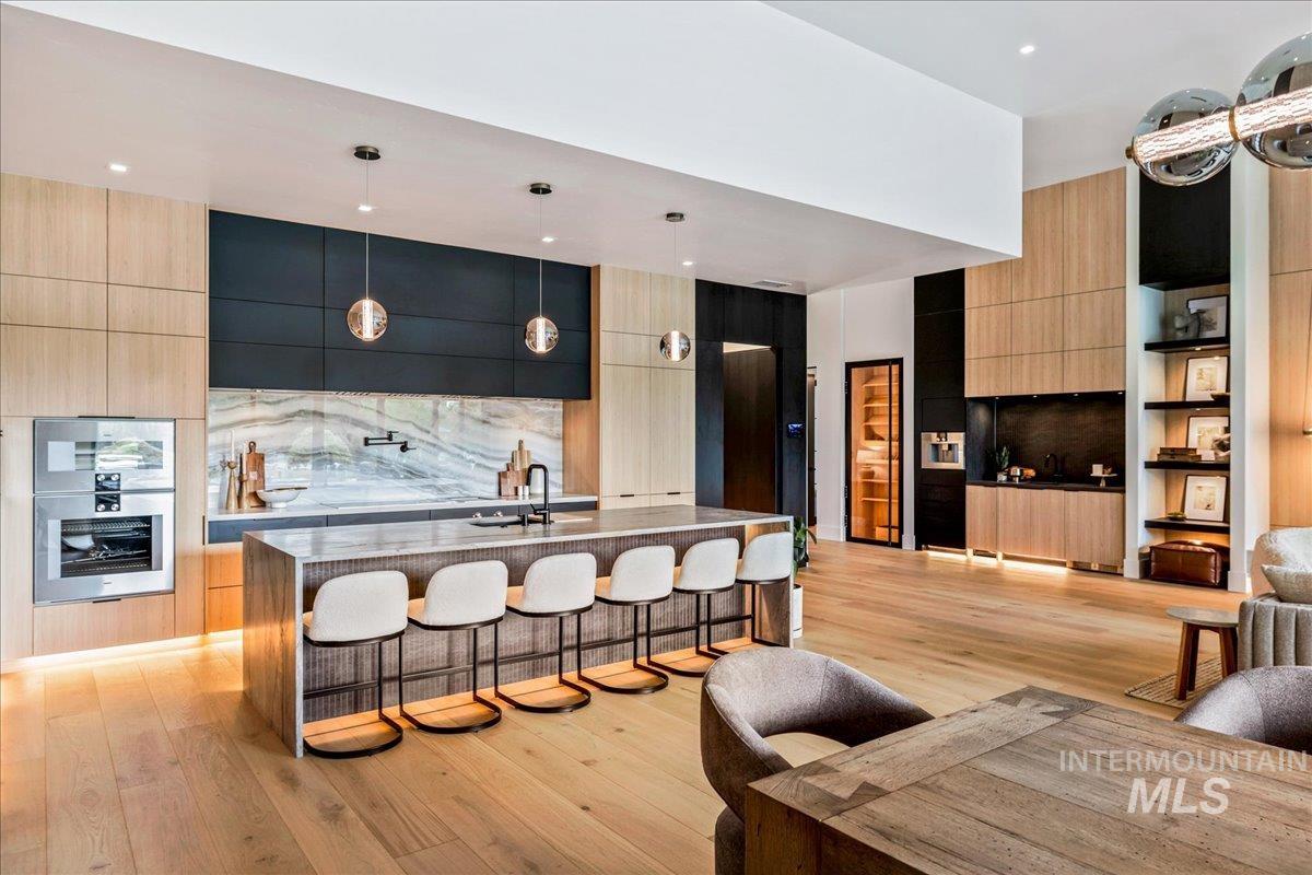 Kitchen with light brown cabinets, modern cabinets, decorative light fixtures, a breakfast bar, and light stone counters