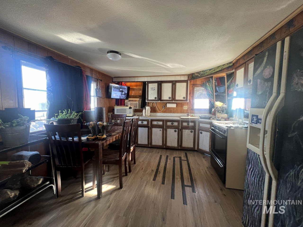 Kitchen featuring refrigerator with ice dispenser, gas range, dark wood-style floors, plenty of natural light, and wood walls