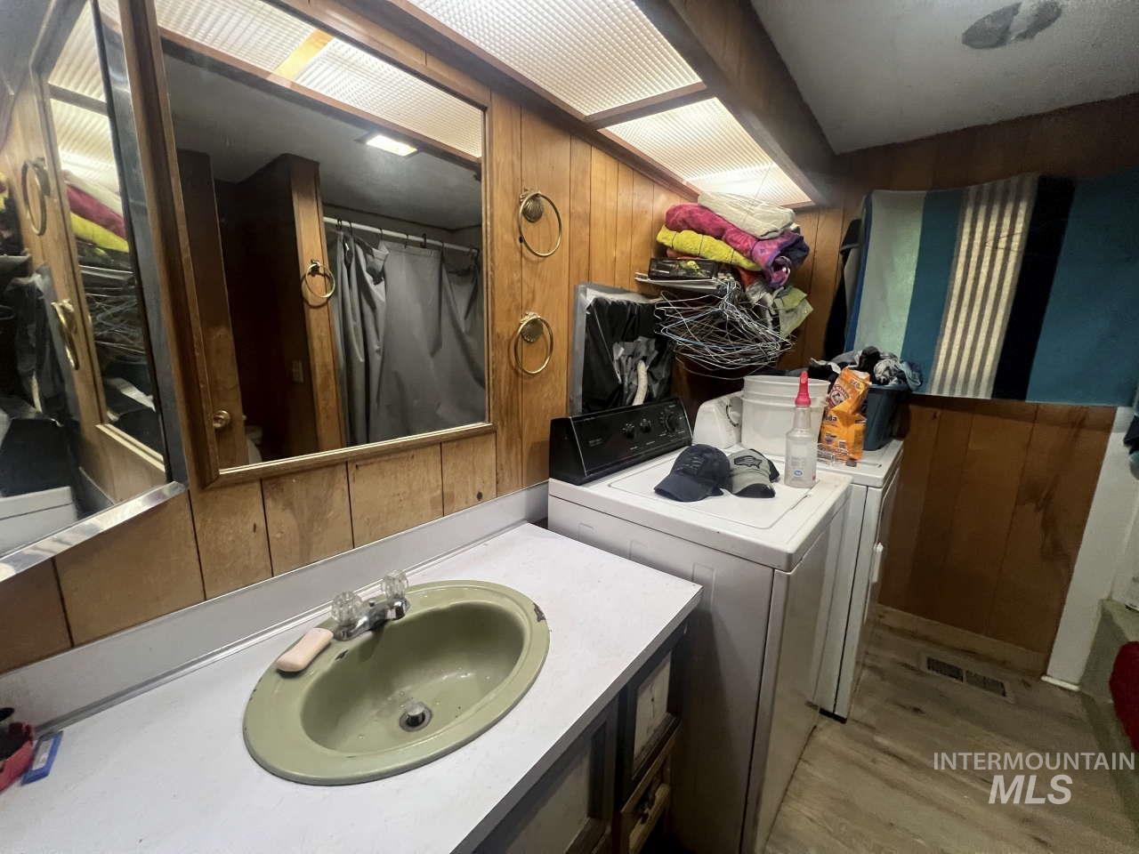 Bathroom with wood walls, vanity, washing machine and clothes dryer, and light wood-style floors