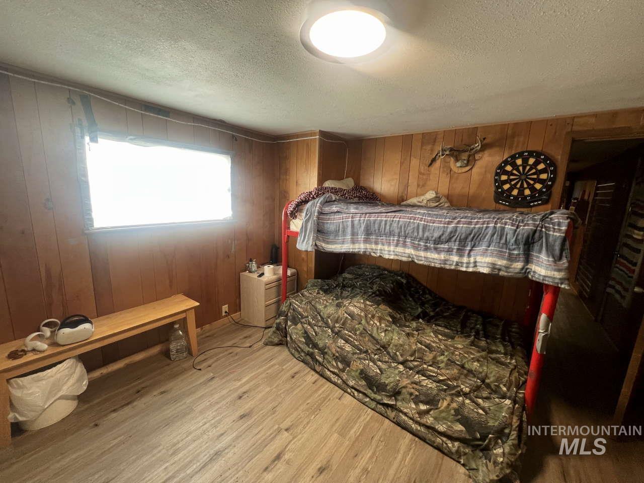 Bedroom featuring wooden walls, a textured ceiling, and wood finished floors
