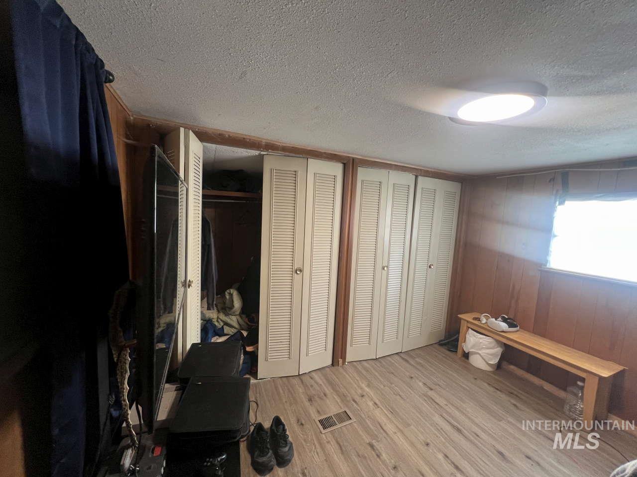 Bedroom featuring two closets, light wood finished floors, wood walls, and a textured ceiling