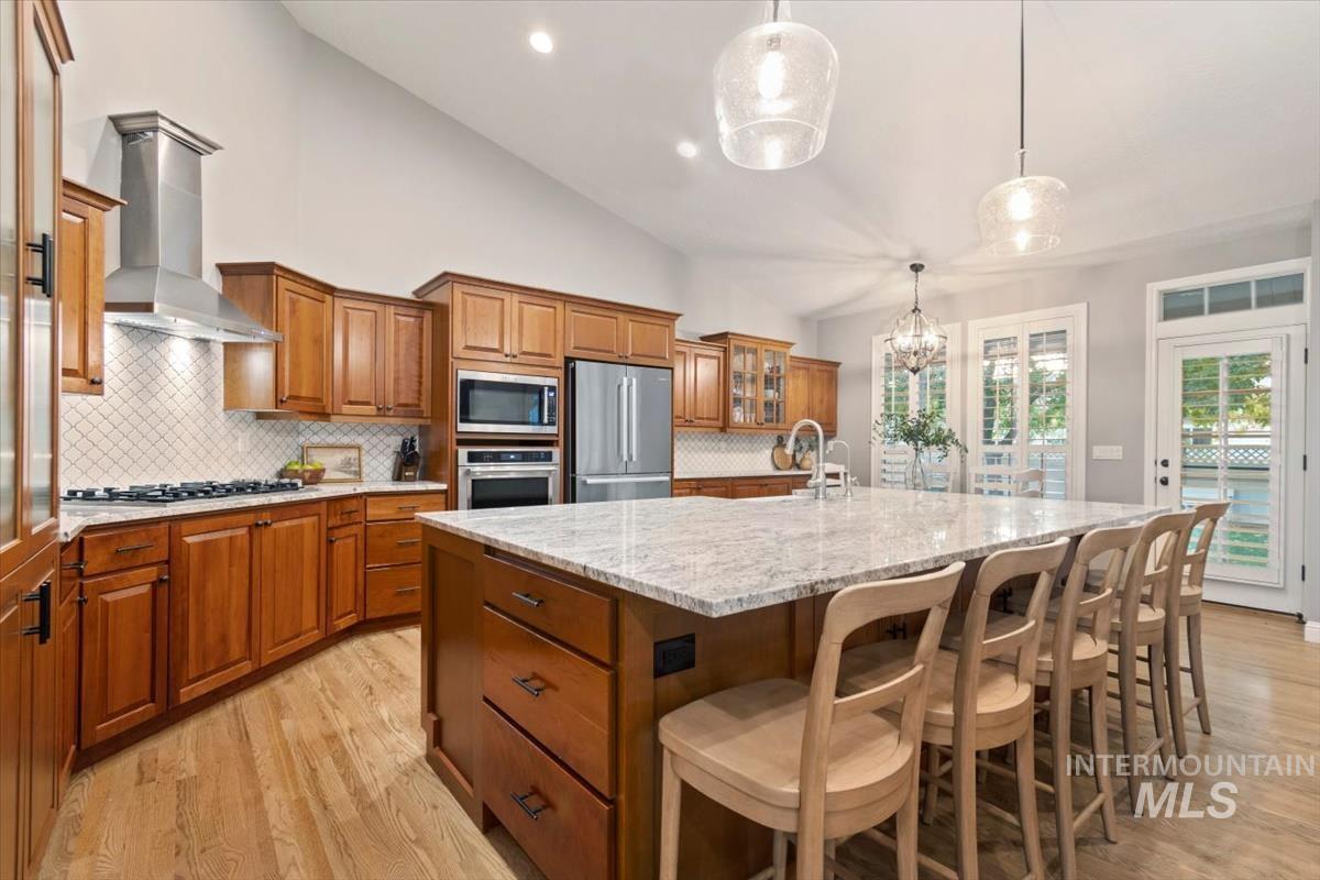 Kitchen with brown cabinets, a large island, backsplash, lofted ceiling, and recessed lighting