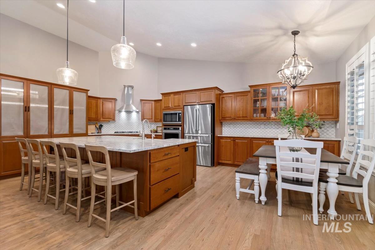 Kitchen featuring glass insert cabinets, brown cabinetry, a breakfast bar area, decorative backsplash, and high vaulted ceiling
