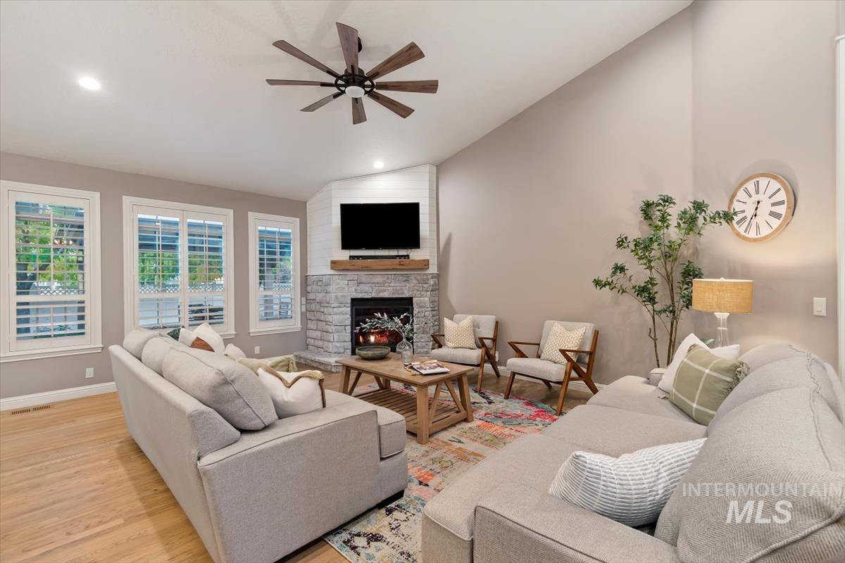 Living area with light wood finished floors, a stone fireplace, ceiling fan, recessed lighting, and high vaulted ceiling