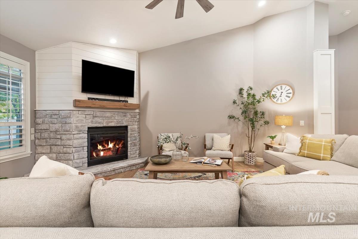 Living area with vaulted ceiling, a stone fireplace, a ceiling fan, wood finished floors, and recessed lighting