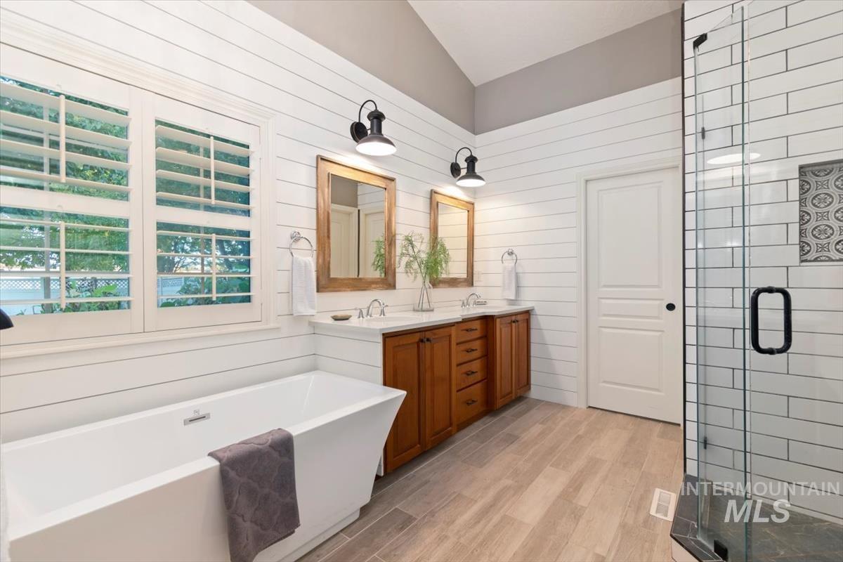 Bathroom with a shower stall, a freestanding bath, double vanity, light wood-style flooring, and vaulted ceiling