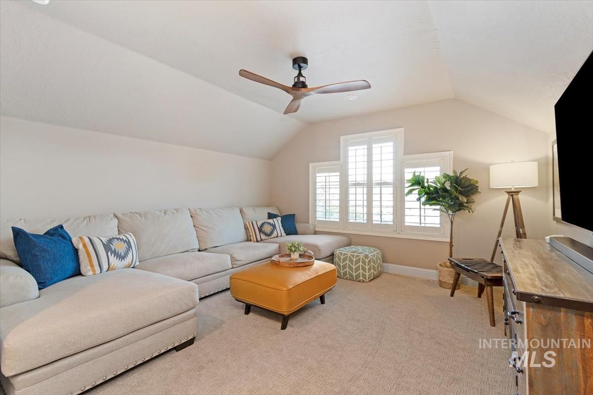 Living area with vaulted ceiling, light colored carpet, and ceiling fan