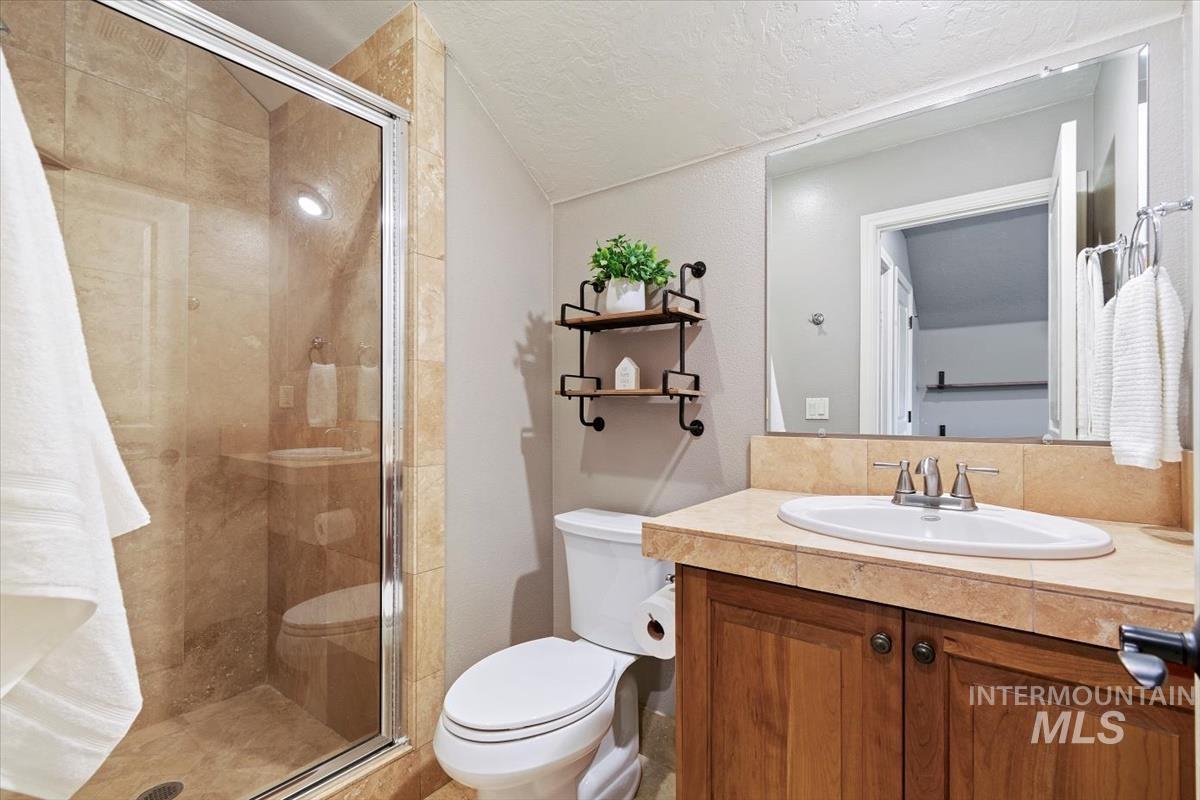 Full bath with a shower stall, vanity, a textured ceiling, and lofted ceiling