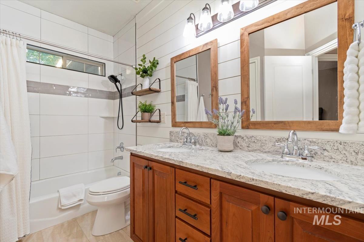 Full bath featuring shower / bath combo, double vanity, and light tile patterned flooring