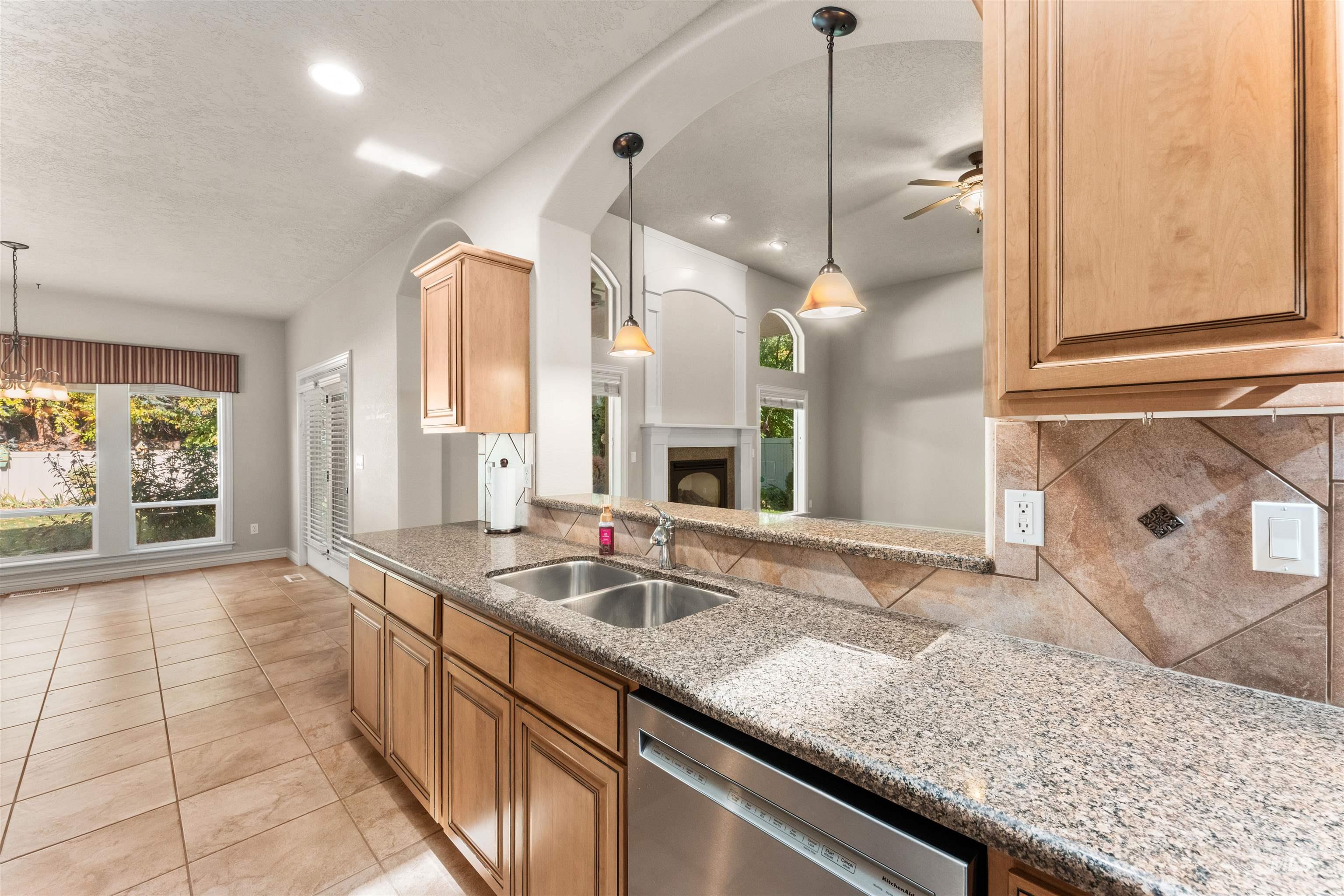 Kitchen featuring pendant lighting, light stone countertops, stainless steel dishwasher, light tile patterned floors, and a textured ceiling
