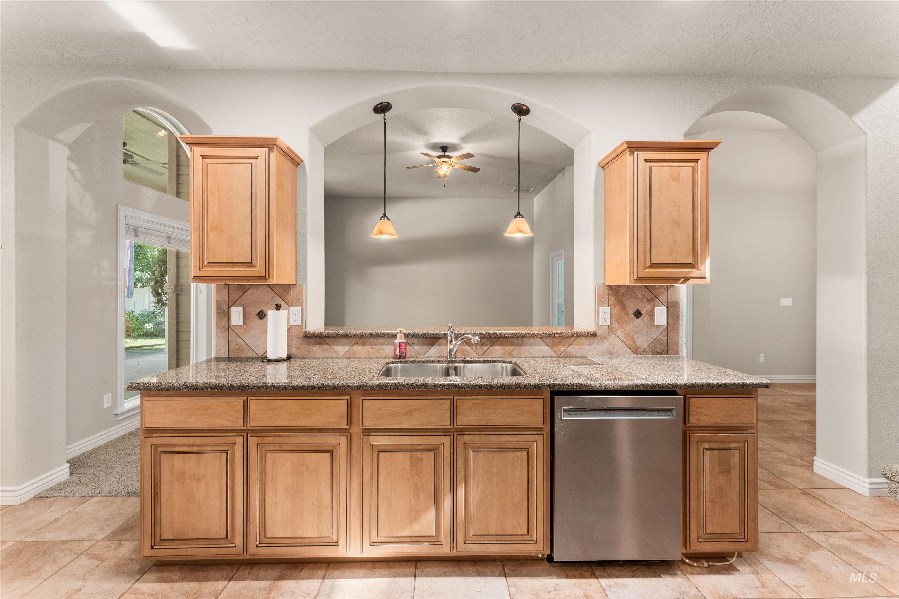 Kitchen featuring backsplash, dishwasher, hanging light fixtures, and arched walkways