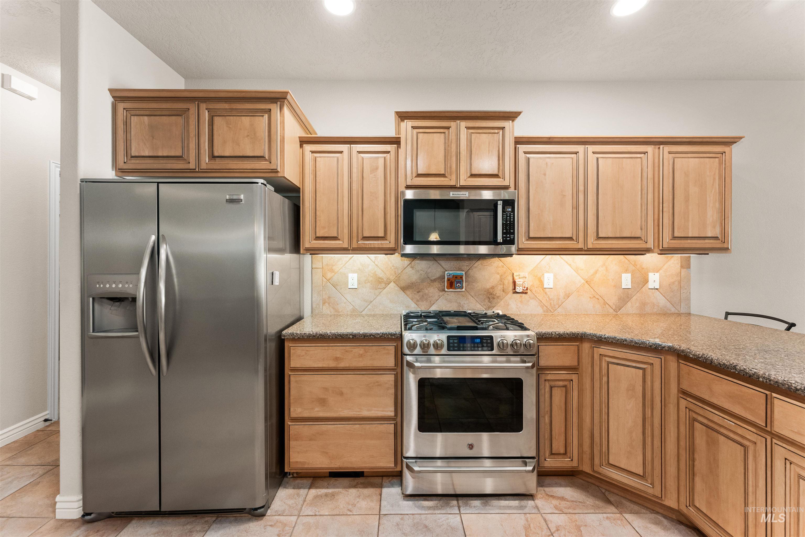 Kitchen featuring appliances with stainless steel finishes, light stone counters, decorative backsplash, light tile patterned flooring, and recessed lighting