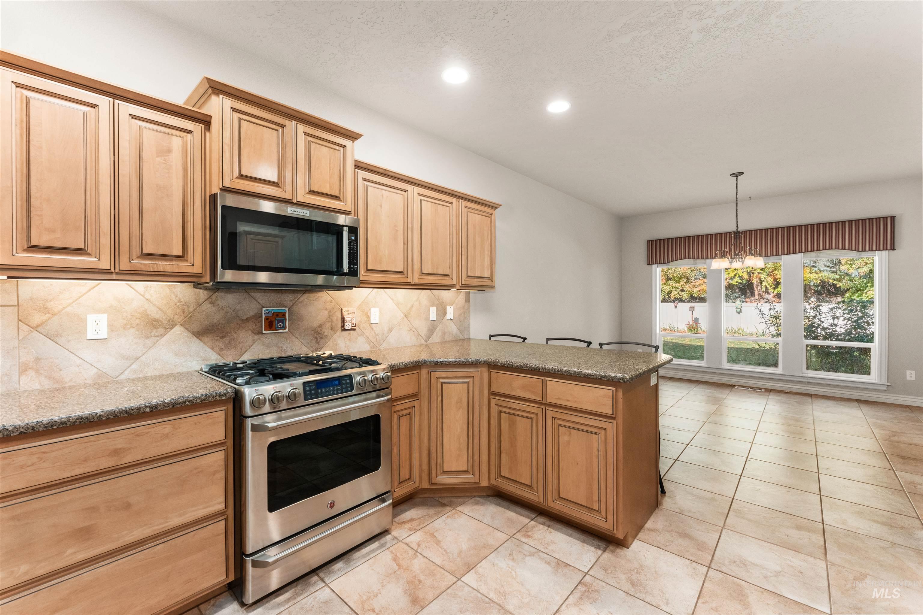 Kitchen with appliances with stainless steel finishes, a peninsula, light stone countertops, decorative light fixtures, and light tile patterned floors