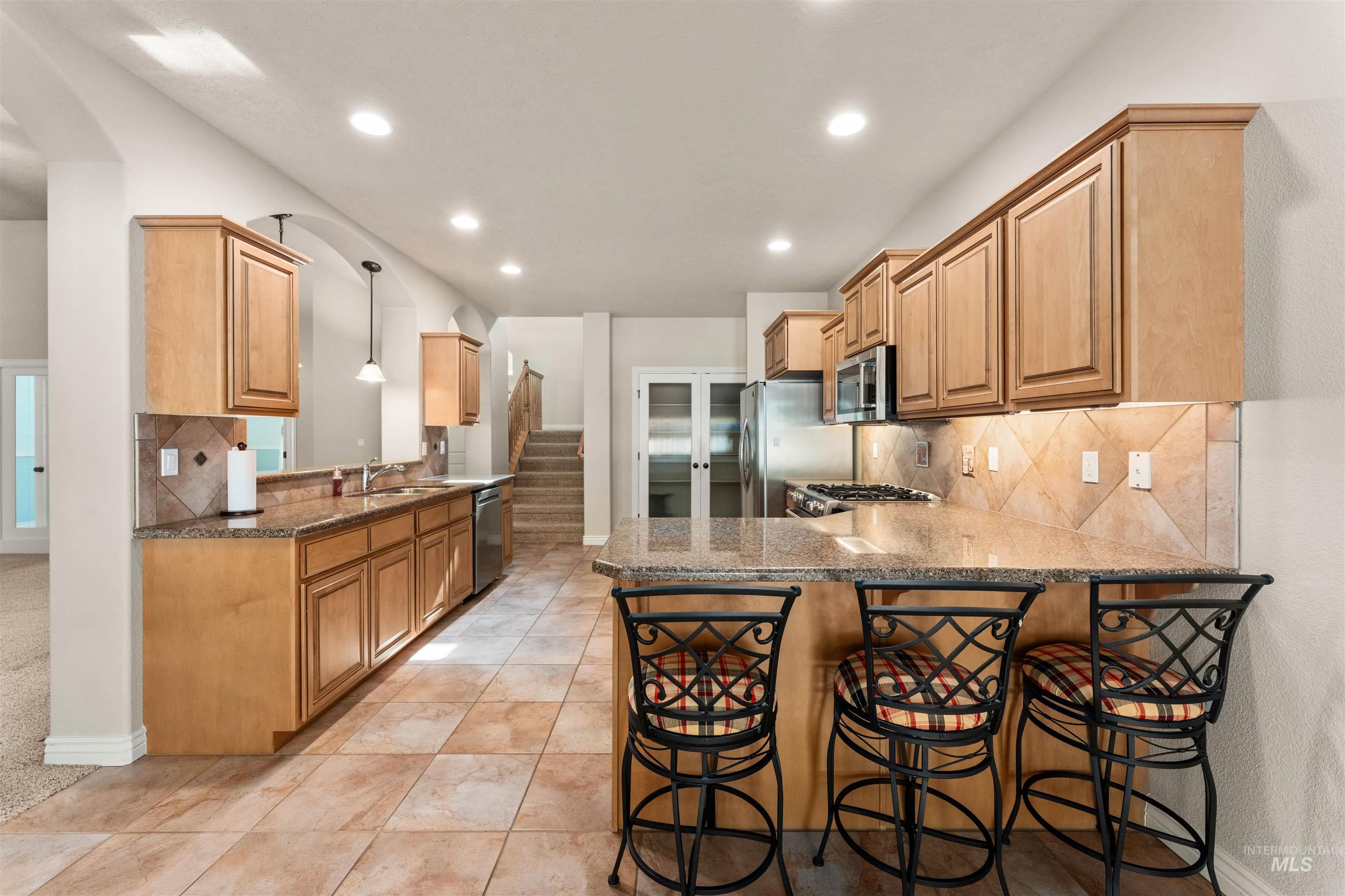 Kitchen with a peninsula, backsplash, a breakfast bar, dark stone counters, and recessed lighting