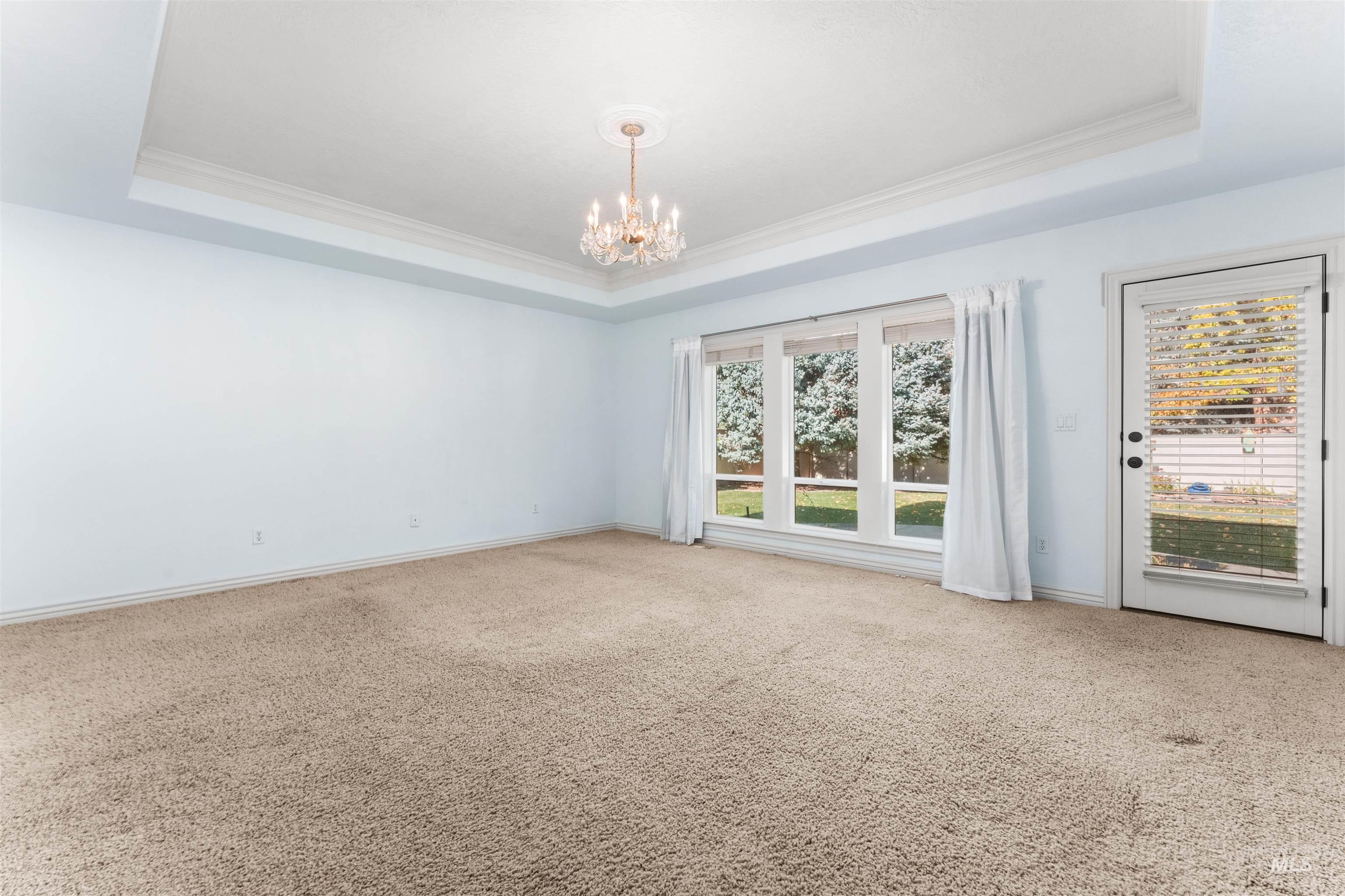 Spare room featuring a tray ceiling, ornamental molding, carpet floors, and a chandelier