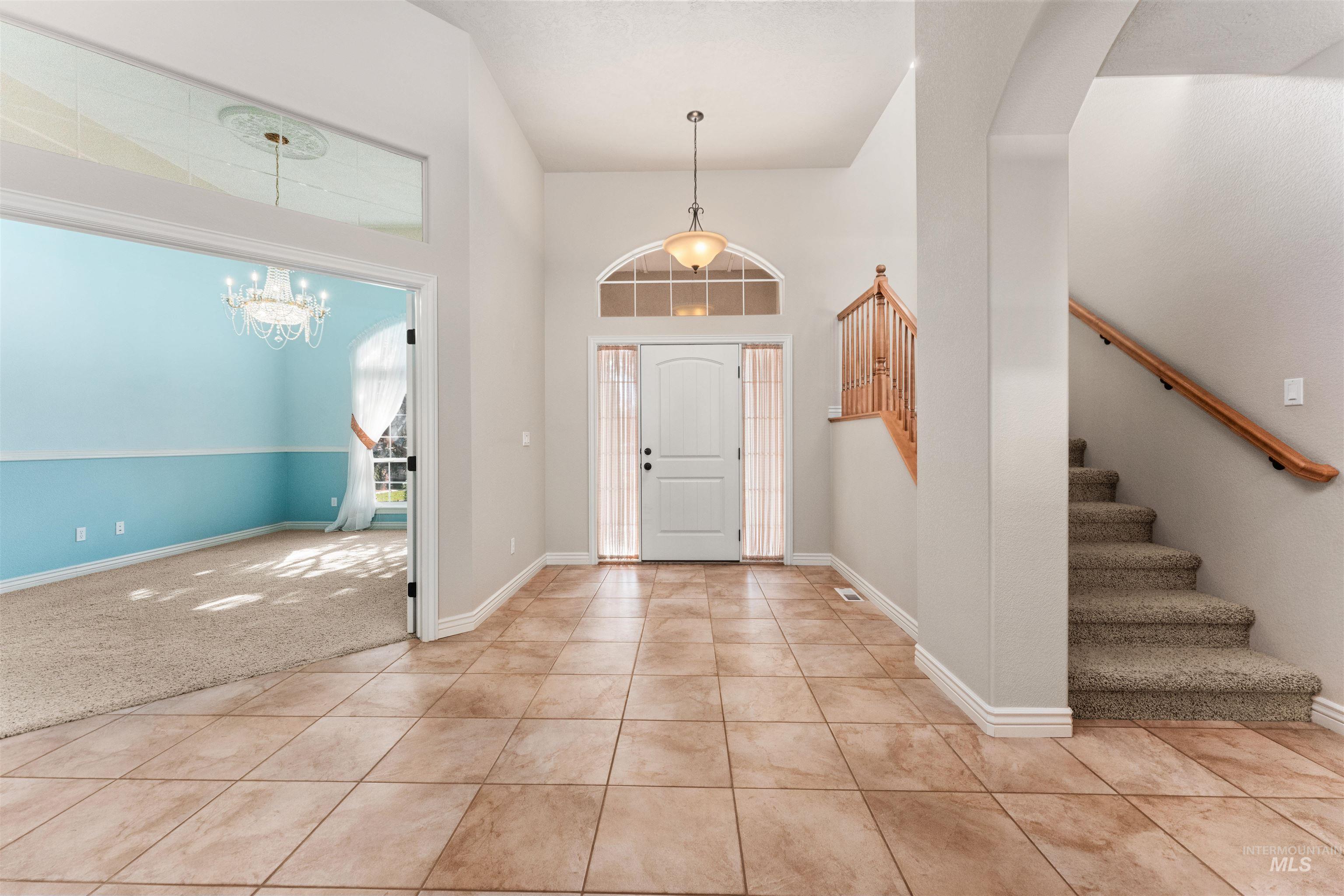 Foyer entrance featuring light tile patterned floors, a high ceiling, stairs, light carpet, and a chandelier