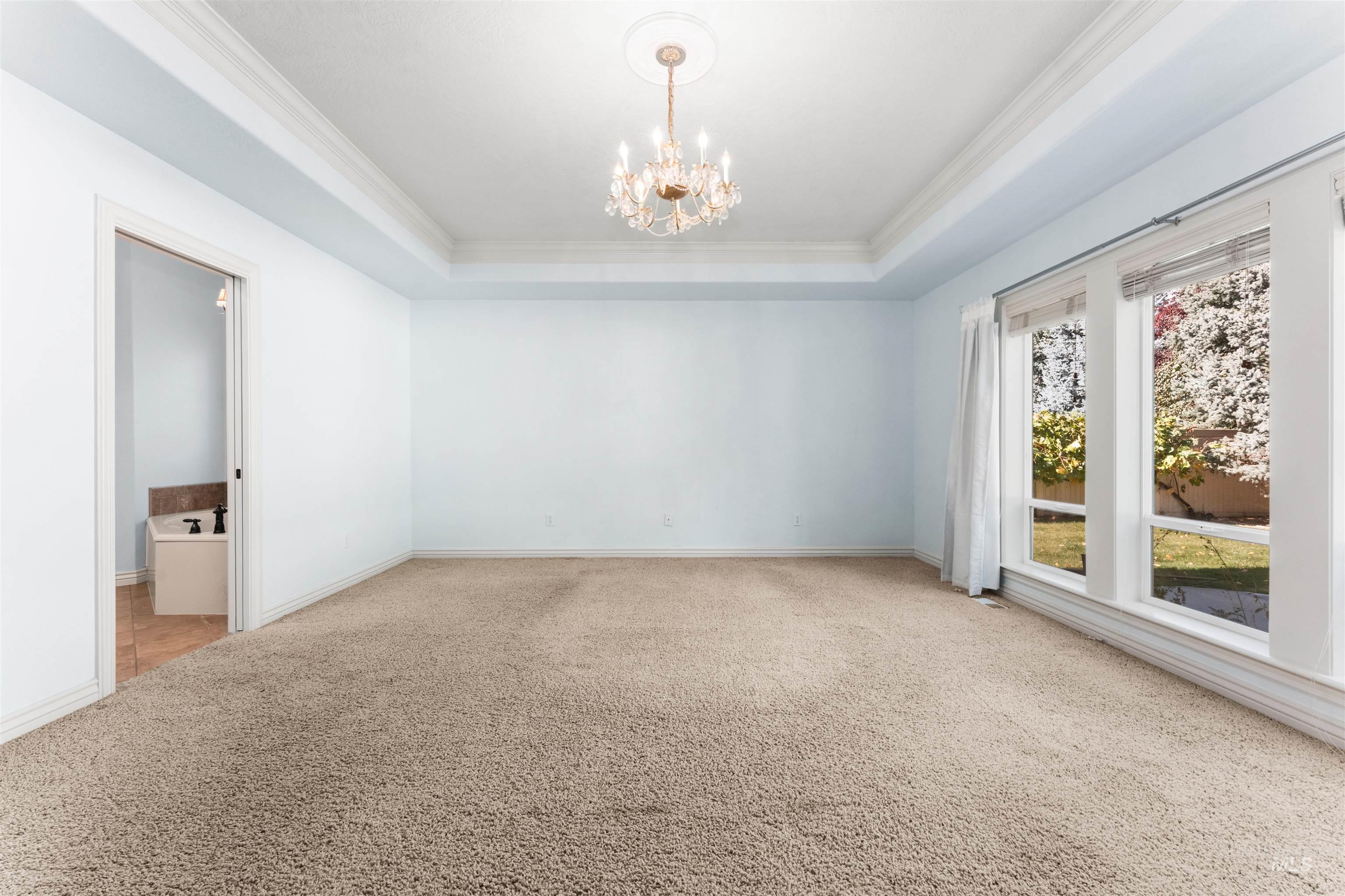 Carpeted empty room with a raised ceiling, ornamental molding, and a chandelier