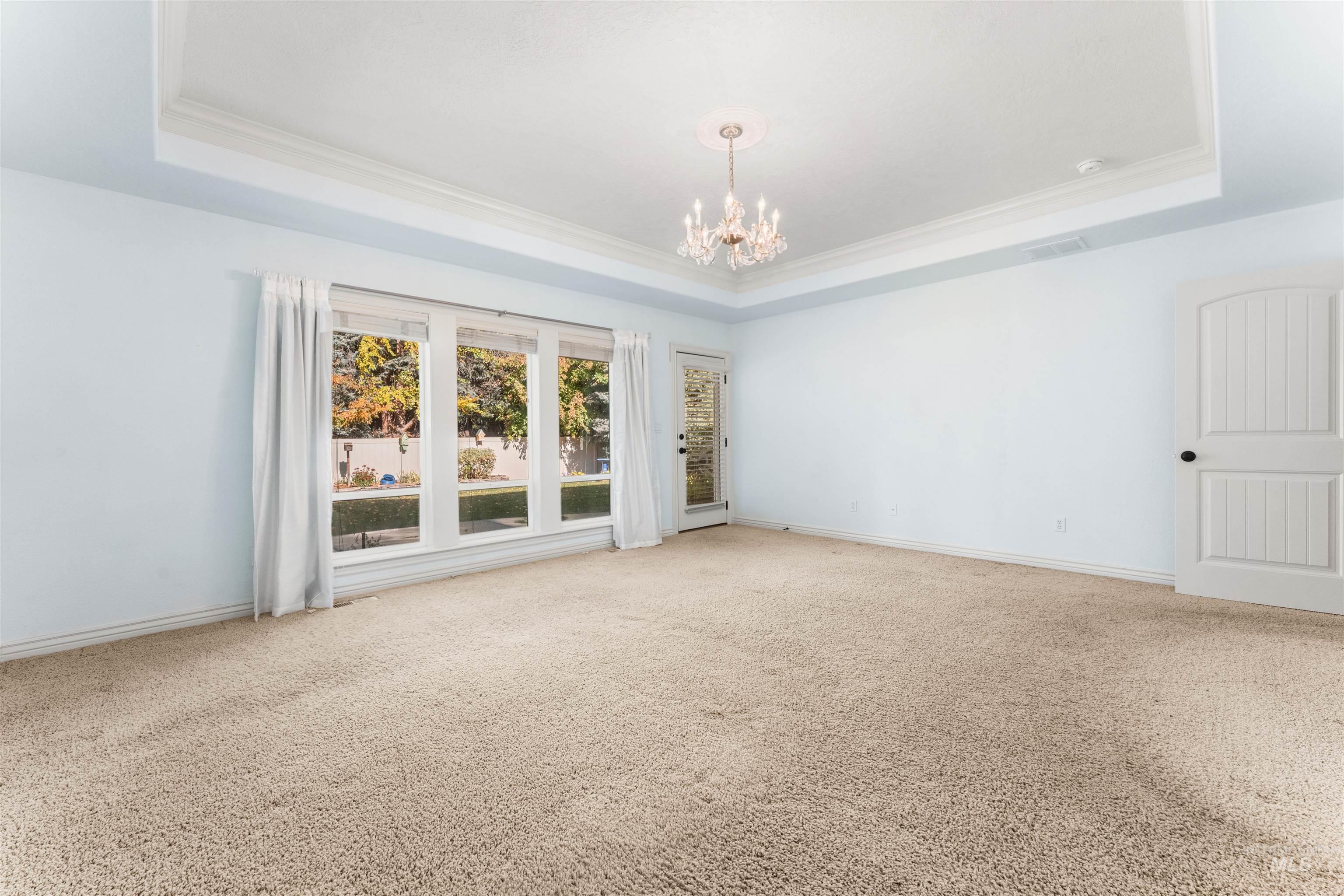 Empty room featuring a raised ceiling, carpet floors, ornamental molding, and a chandelier