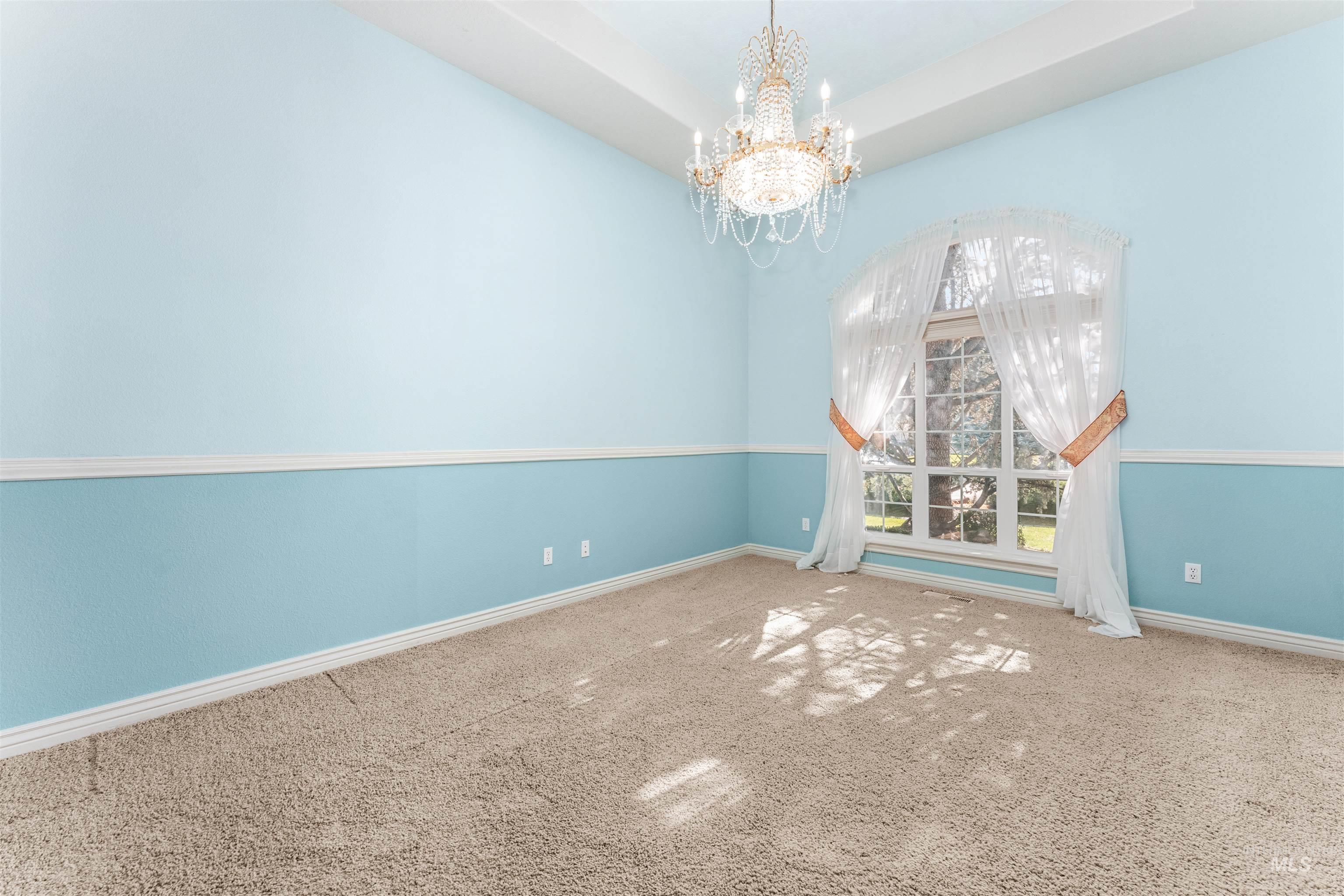 Empty room featuring a chandelier, a raised ceiling, carpet floors, and a towering ceiling