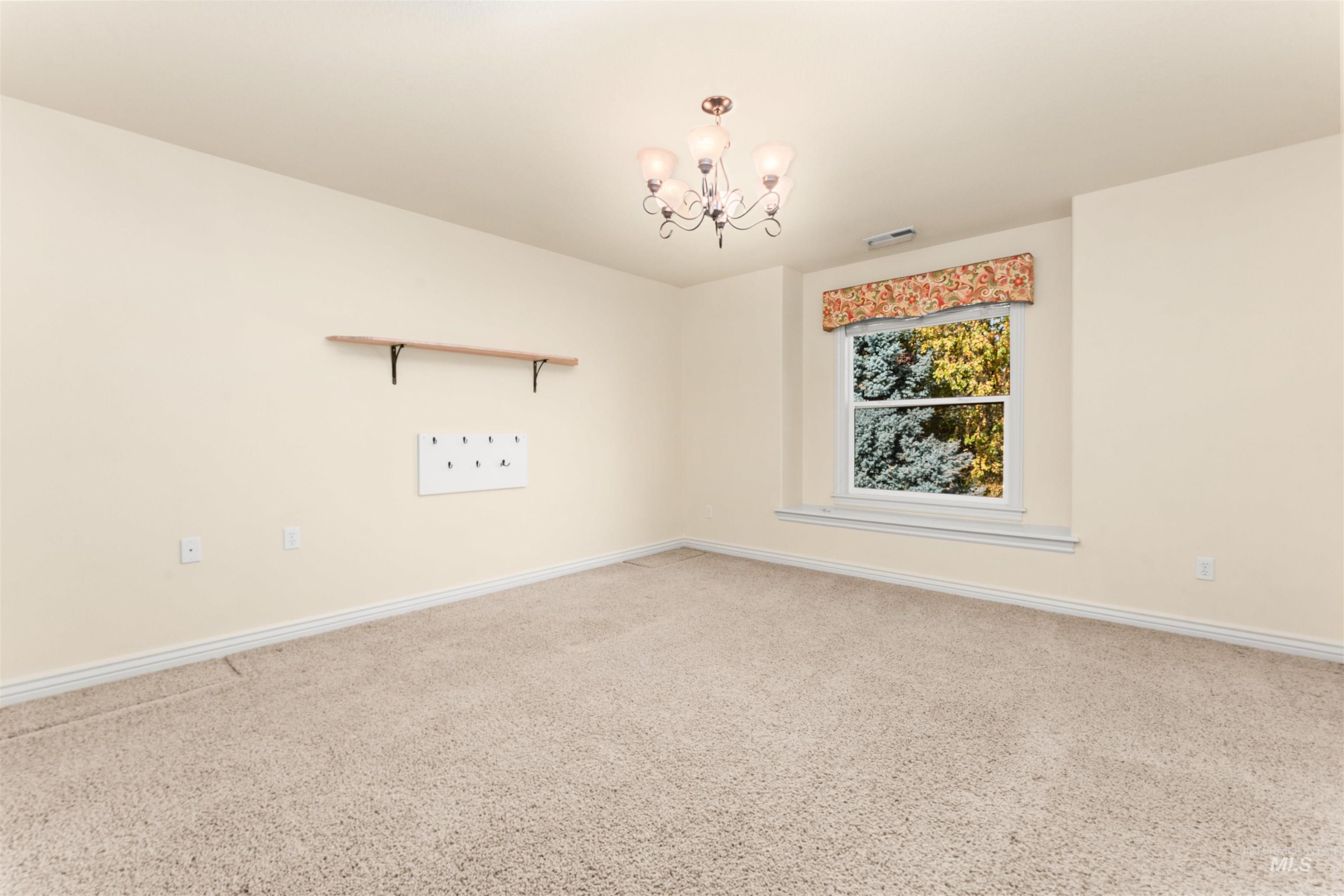 Carpeted spare room featuring baseboards and a chandelier