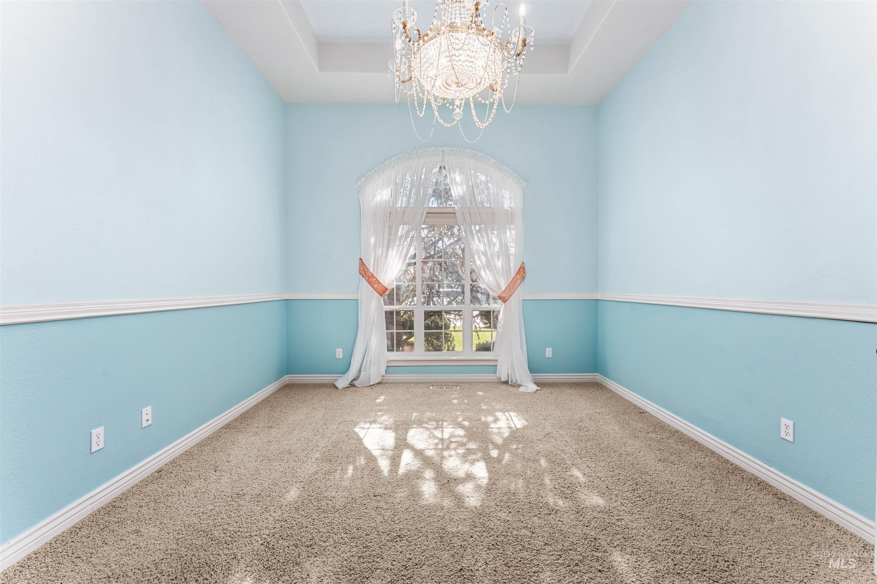 Spare room with carpet, a chandelier, and a raised ceiling