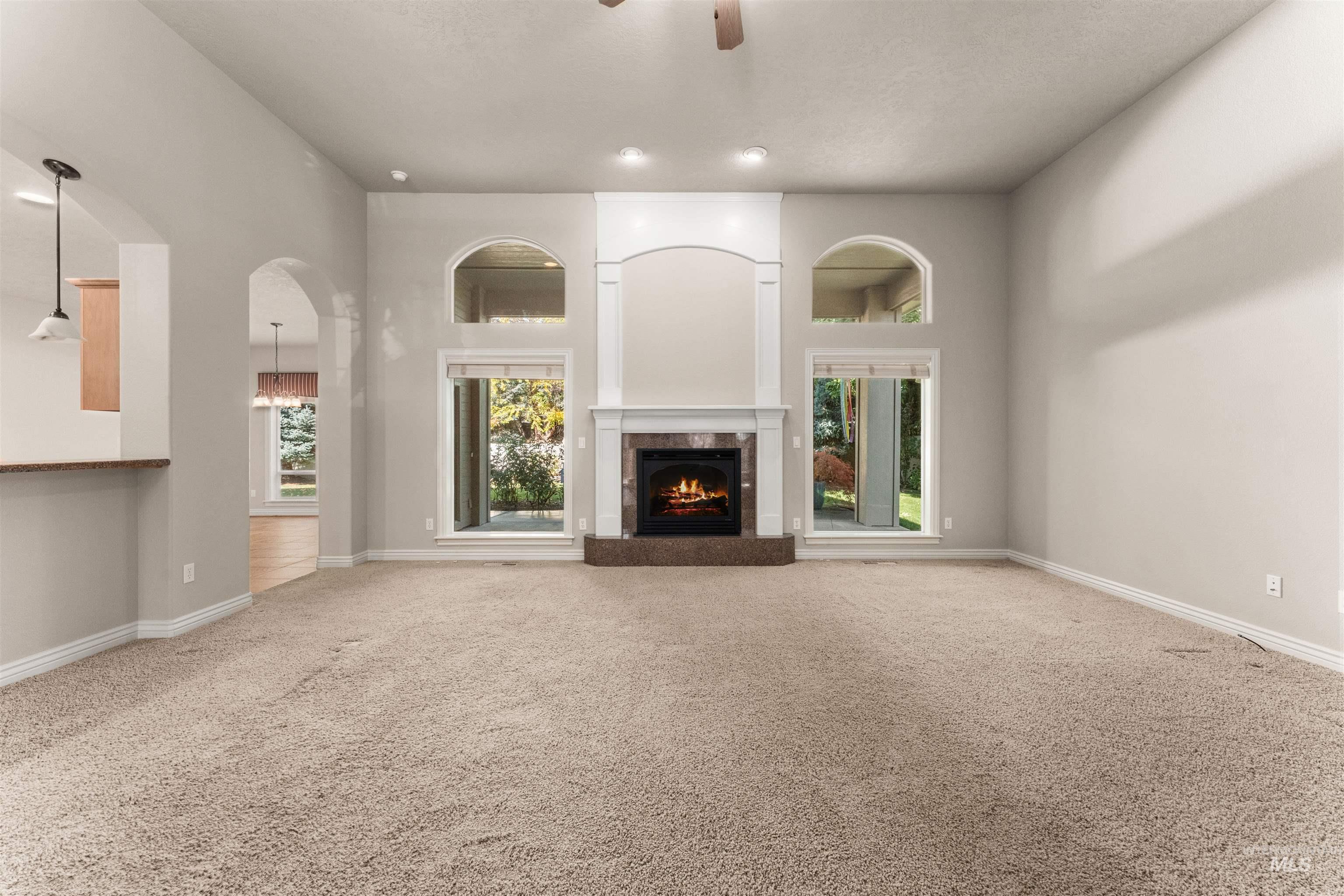 Unfurnished living room with carpet flooring, ceiling fan, a tile fireplace, healthy amount of natural light, and a towering ceiling