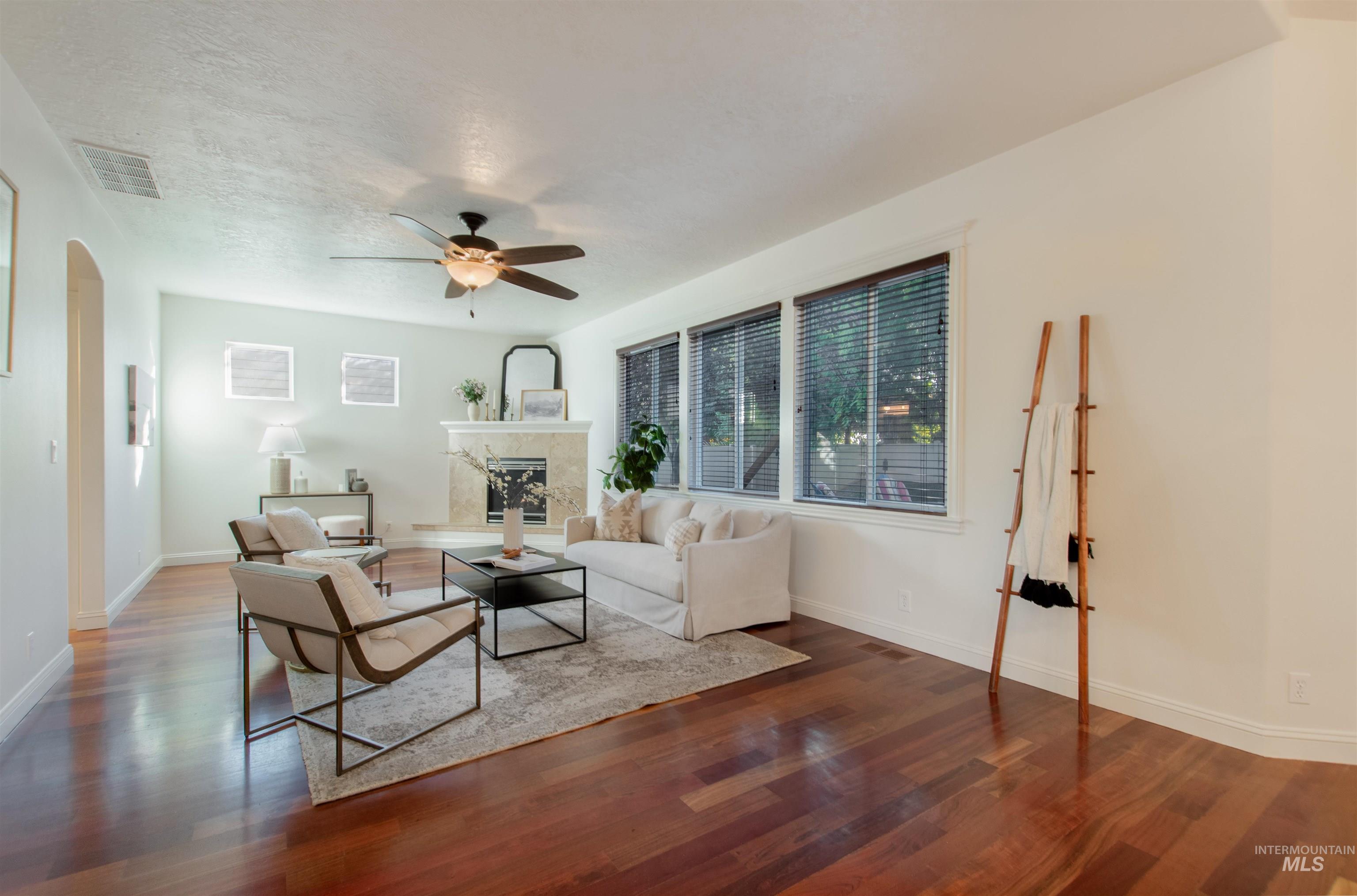 Living area featuring arched walkways, a fireplace, wood finished floors, a ceiling fan, and a textured ceiling