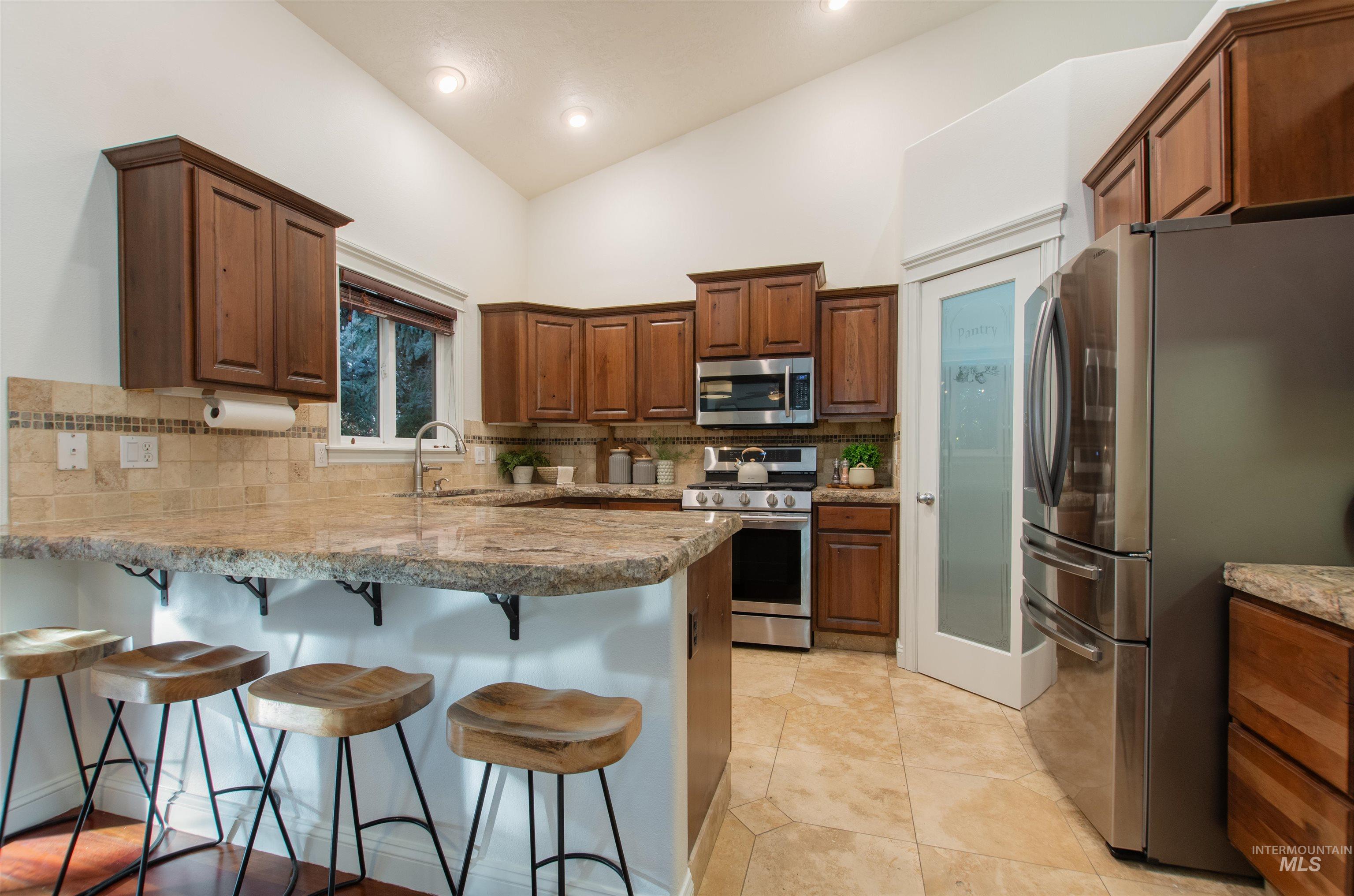 Kitchen with stainless steel appliances, a peninsula, lofted ceiling, backsplash, and a breakfast bar