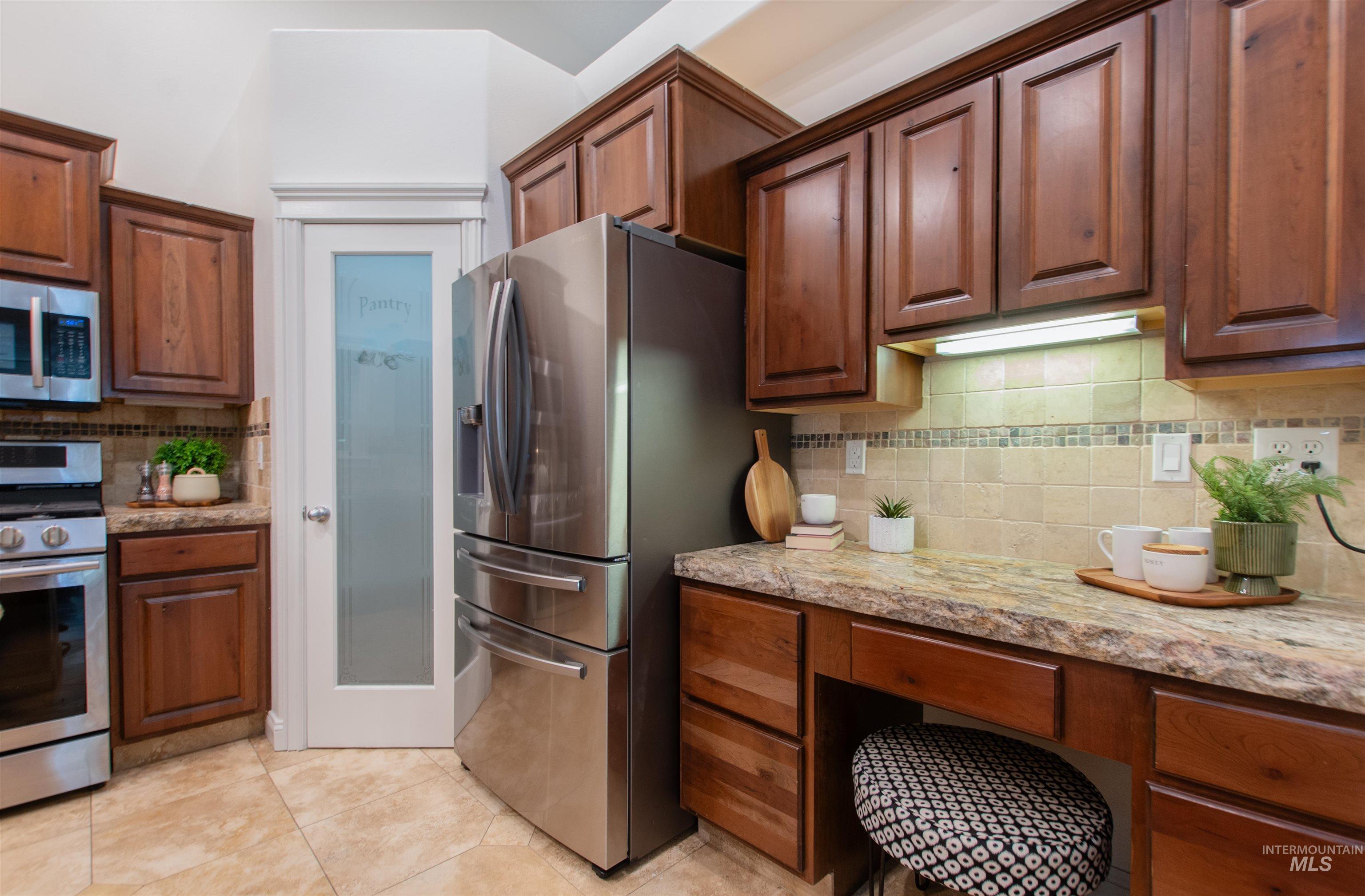 Kitchen featuring decorative backsplash, stainless steel appliances, light stone counters, and light tile patterned floors