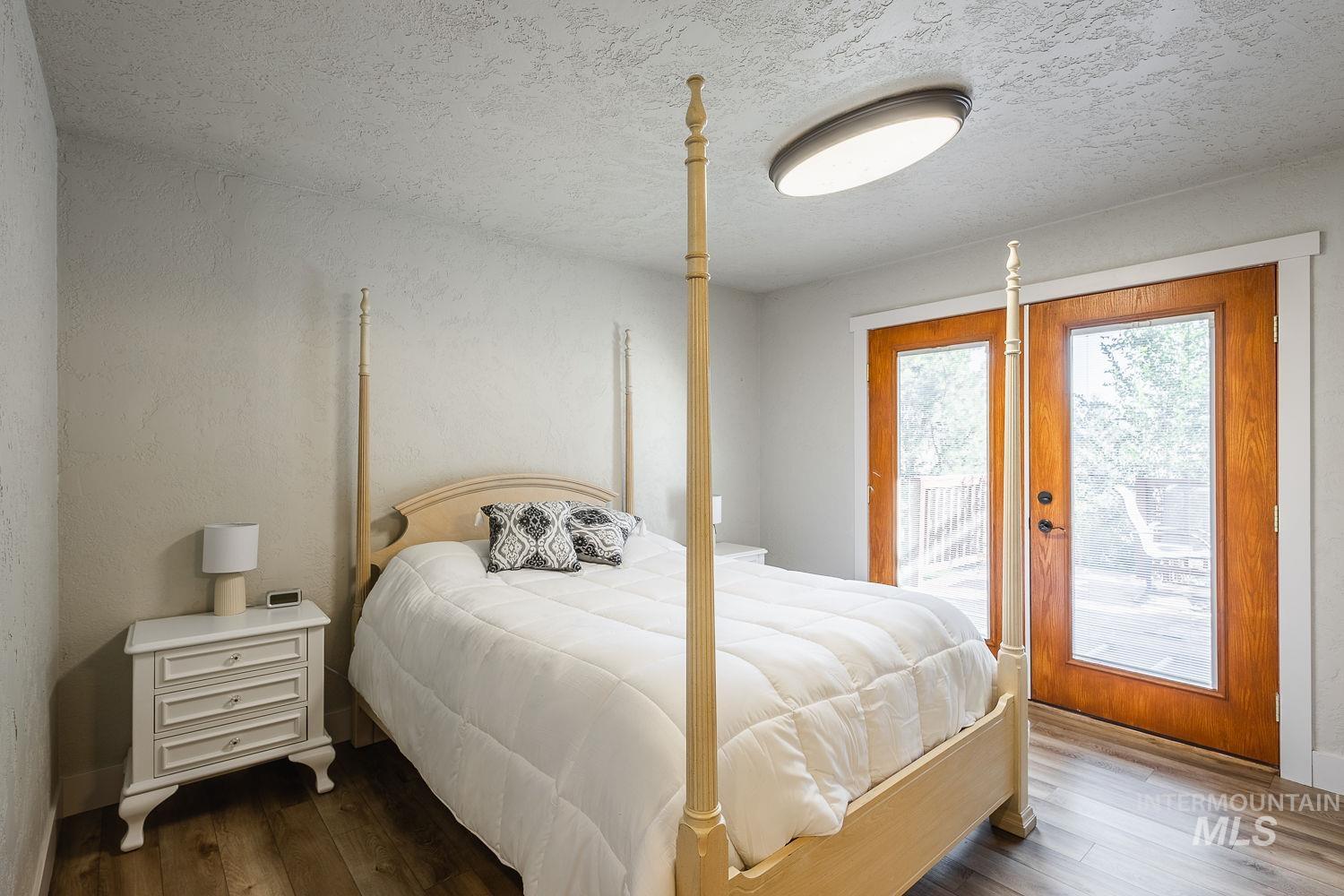 Bedroom with a textured ceiling, dark wood-type flooring, access to outside, and a textured wall