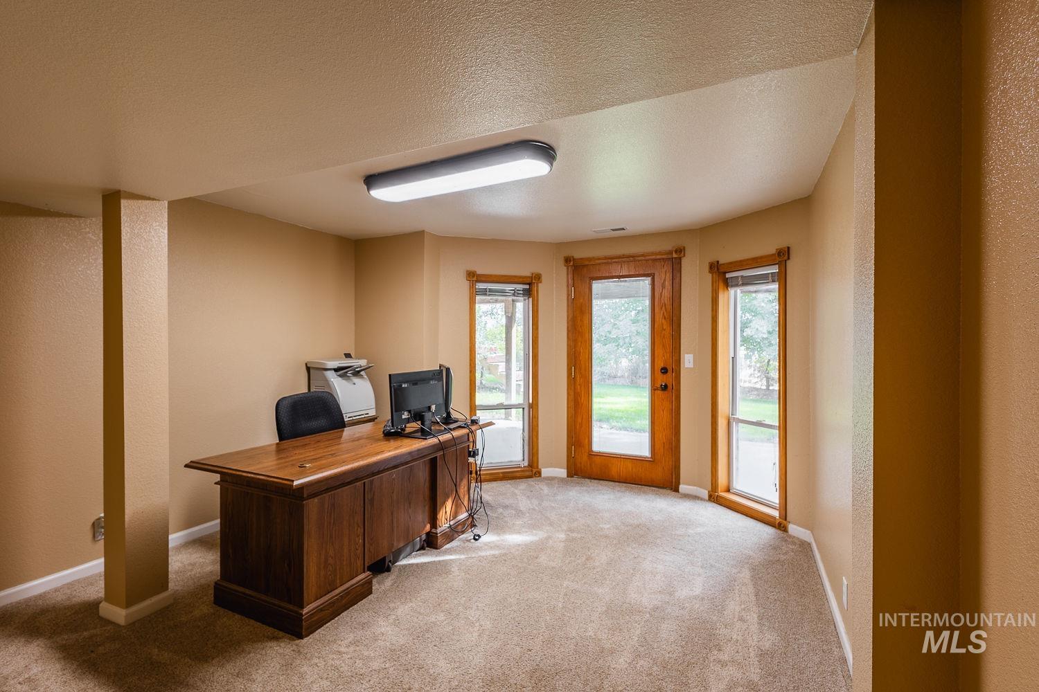 Home office featuring a textured wall, a textured ceiling, and light carpet