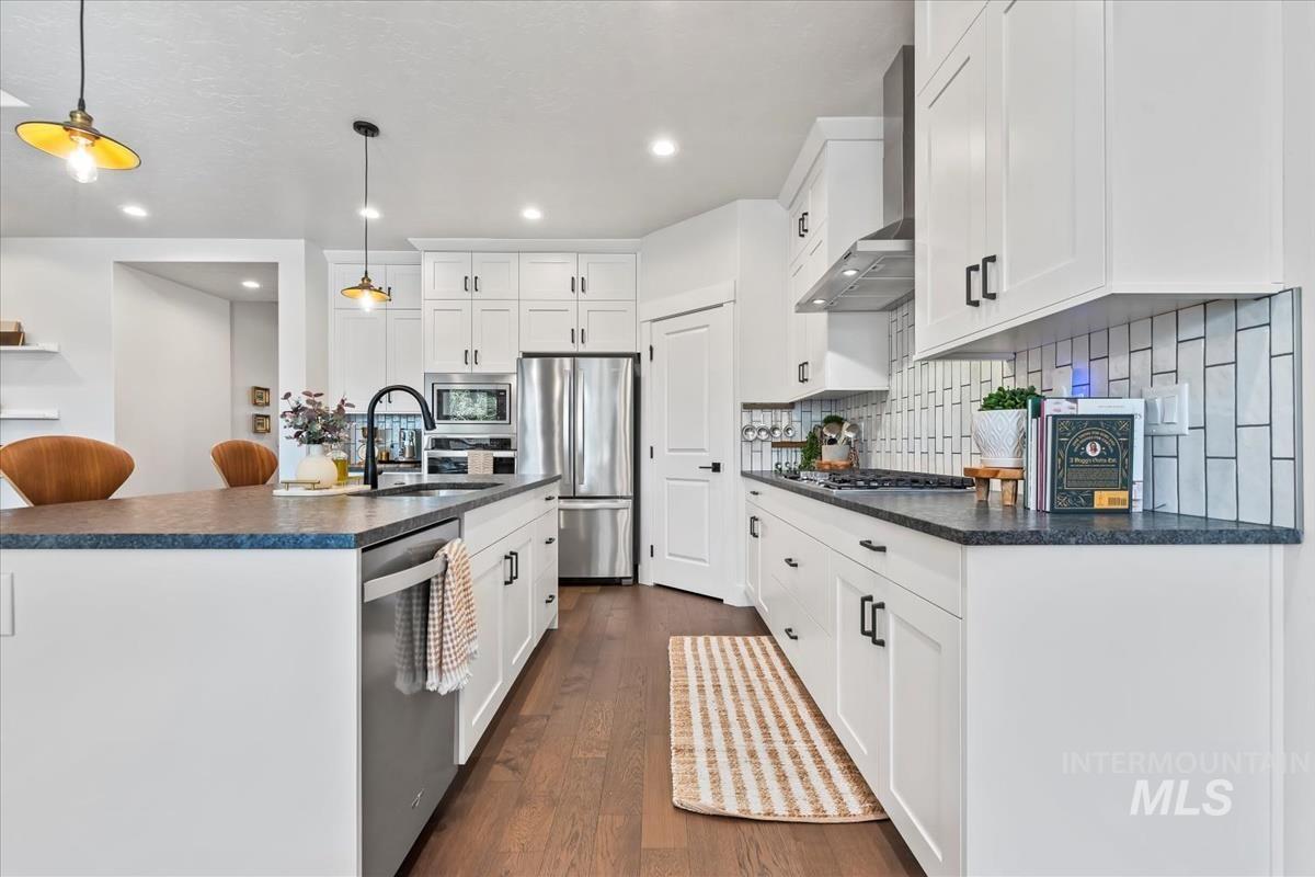 Kitchen featuring dark wood-style floors, appliances with stainless steel finishes, white cabinets, a kitchen island with sink, and decorative light fixtures