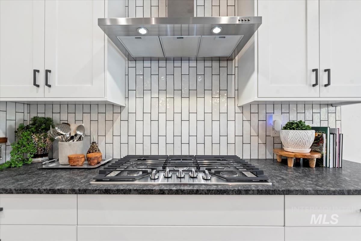 Kitchen featuring wall chimney range hood, stainless steel gas cooktop, tasteful backsplash, and white cabinetry