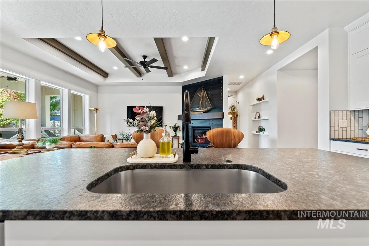 Kitchen featuring open floor plan, pendant lighting, dark stone counters, white cabinetry, and decorative backsplash