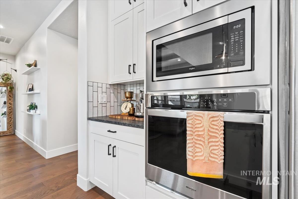 Kitchen featuring appliances with stainless steel finishes, white cabinets, dark stone counters, dark wood-type flooring, and decorative backsplash