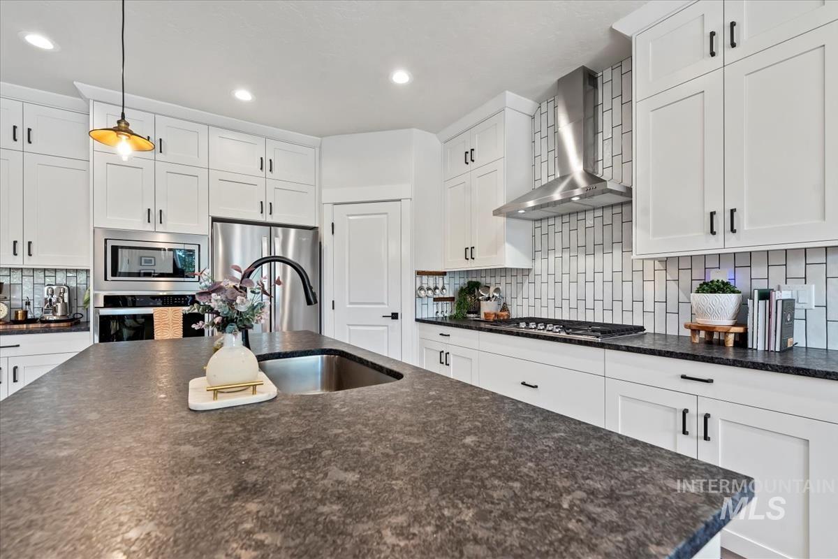 Kitchen with backsplash, white cabinets, wall chimney exhaust hood, hanging light fixtures, and stainless steel appliances