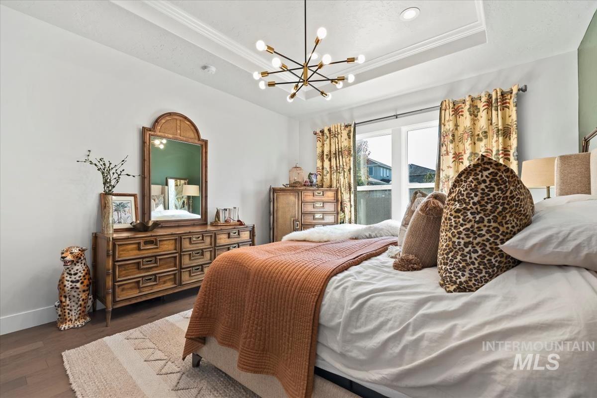 Bedroom with a raised ceiling, wood finished floors, a chandelier, and ornamental molding