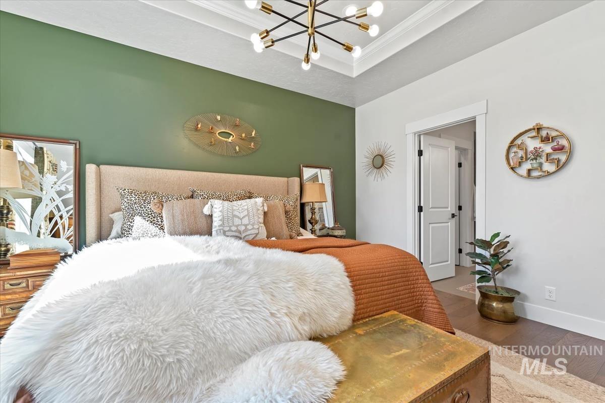 Bedroom with a chandelier, a raised ceiling, wood finished floors, and crown molding
