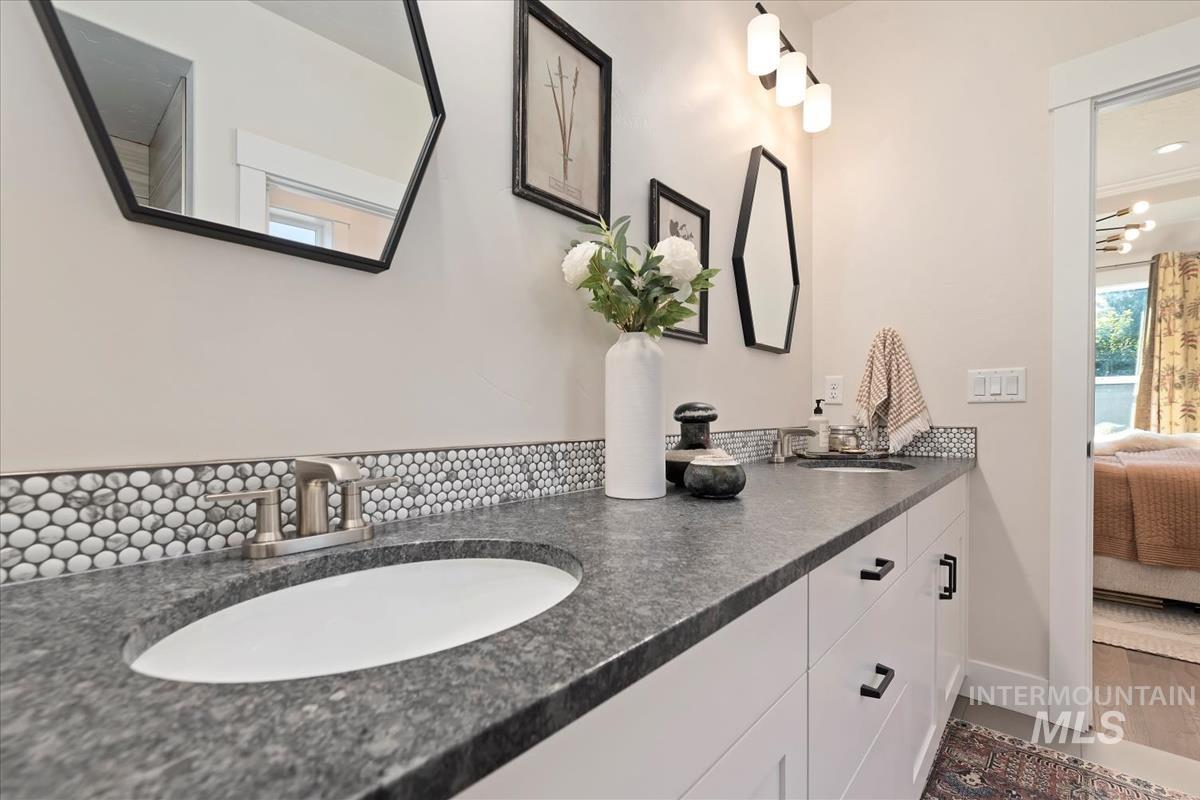 Ensuite bathroom featuring double vanity, decorative backsplash, and wood finished floors